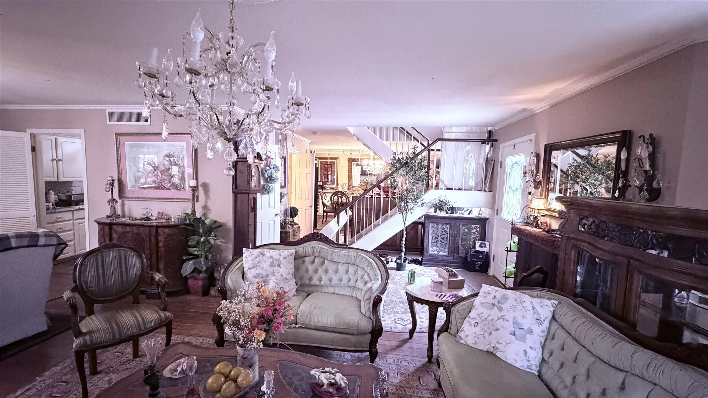 Grand living area featuring a crystal chandelier, wood-finish flooring, and a staircase with wood railings