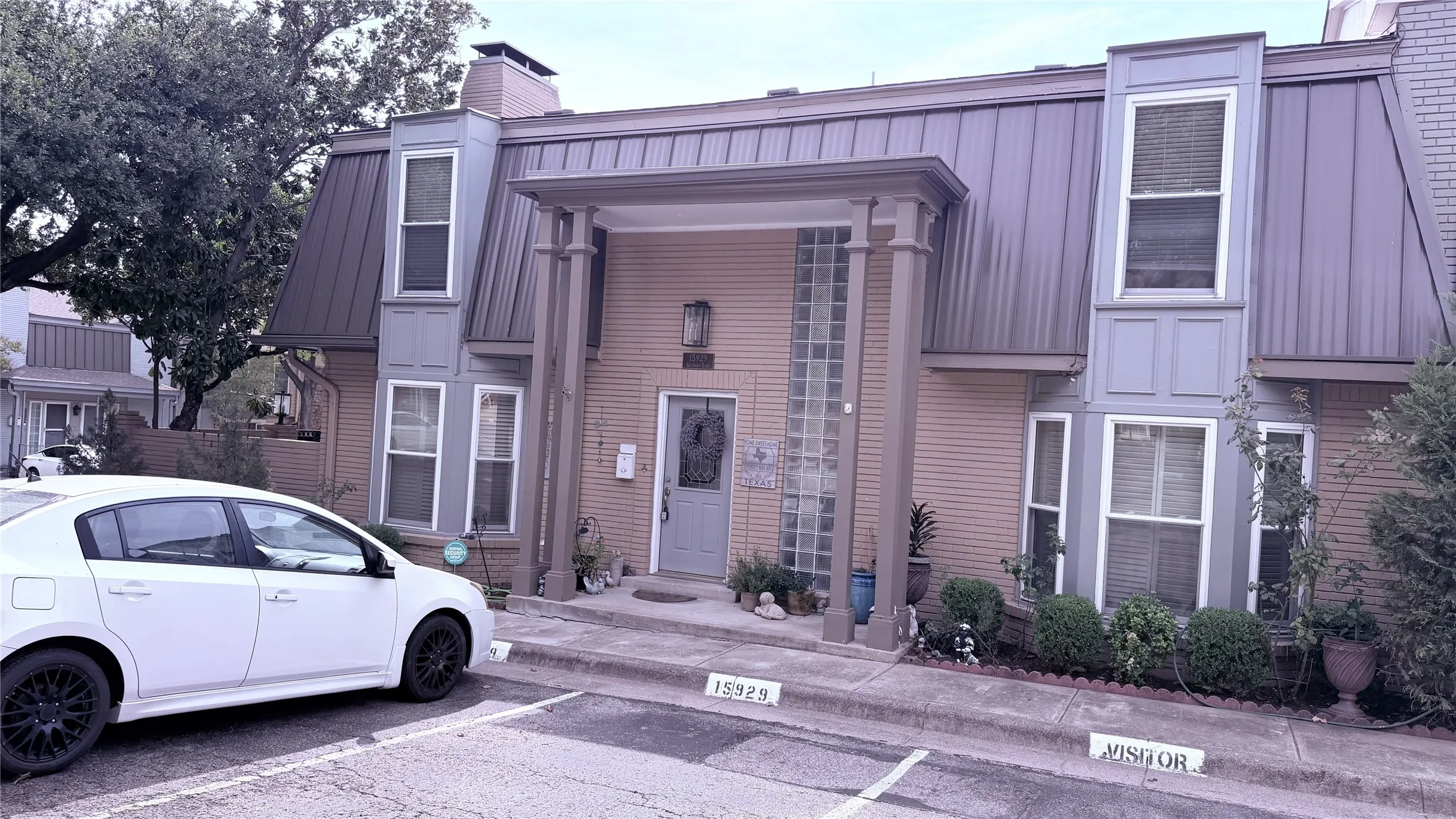 Brick exterior with a metal roof, featuring a covered entry, decorative columns, and a large glass block window