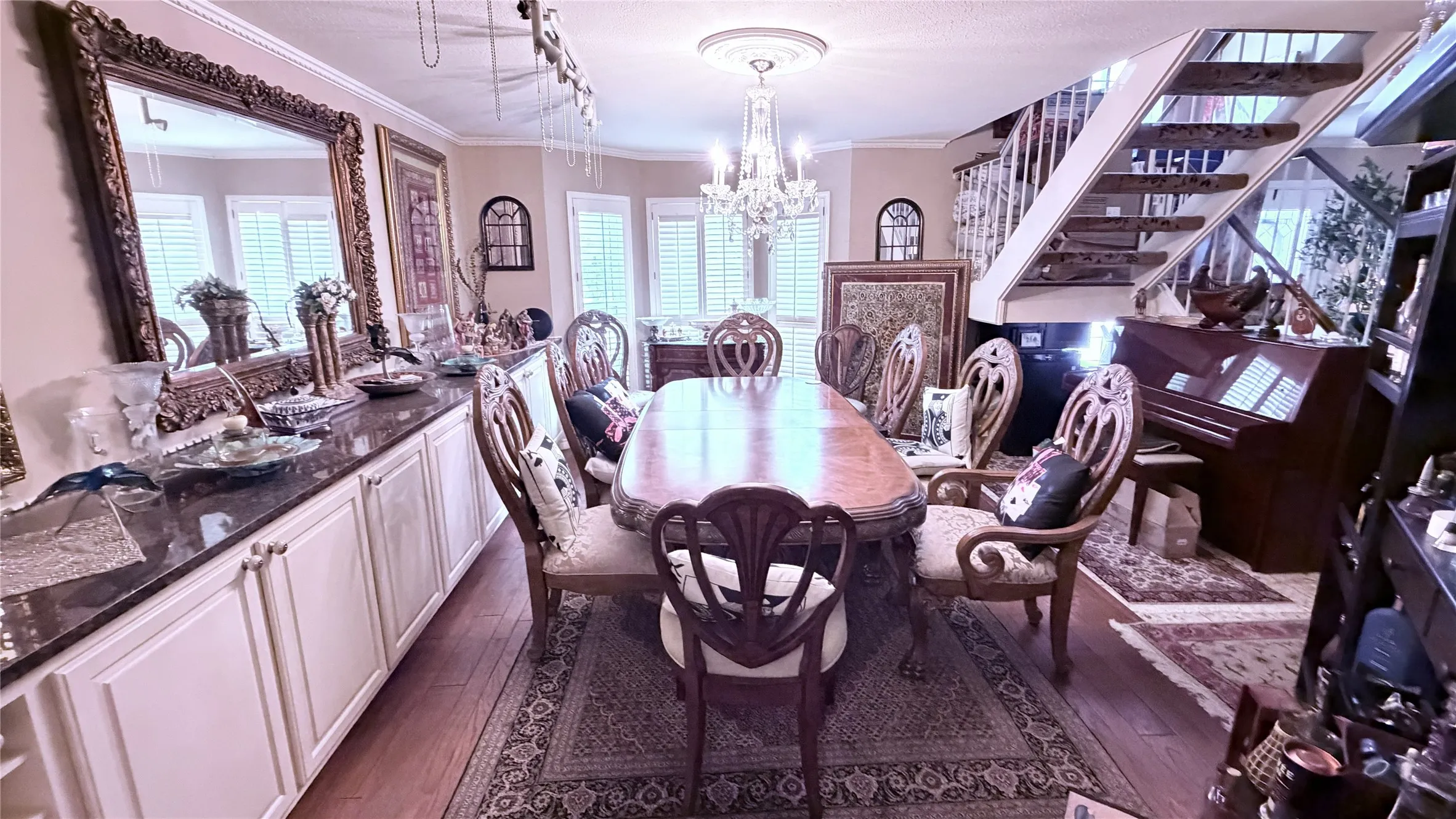 Hardwood flooring, built-in cabinetry with dark countertops, chandelier lighting, and a staircase with white balusters