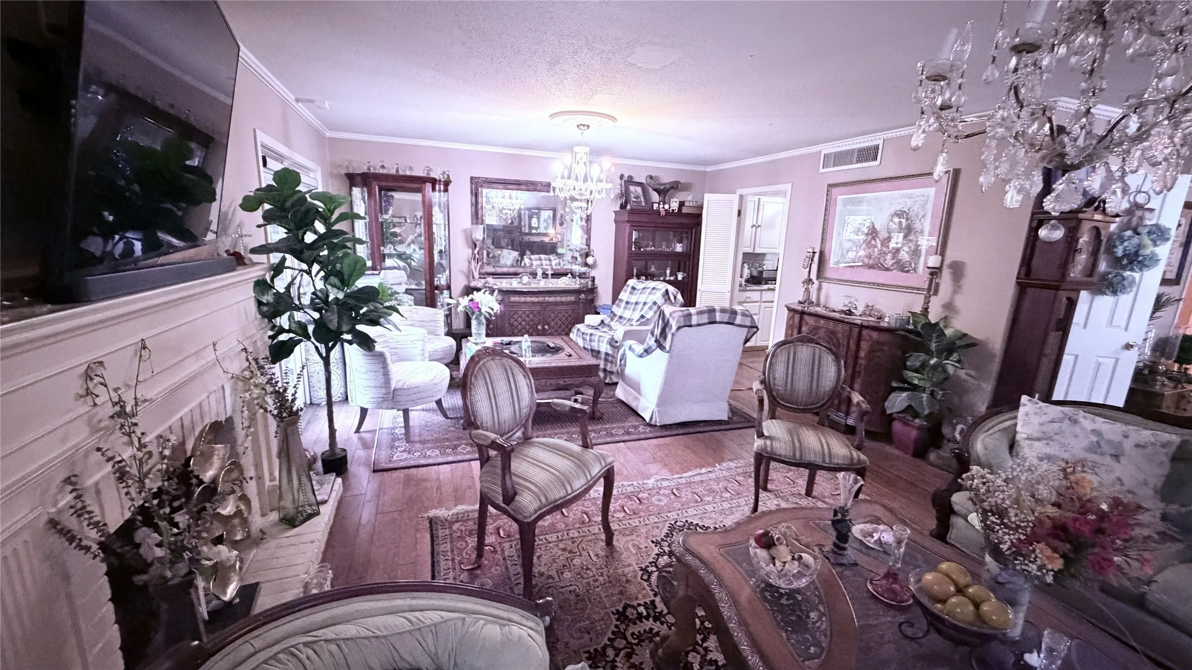 Hardwood-finish flooring, a decorative chandelier, a detailed fireplace with a mantel, crown molding, and built-in cabinetry