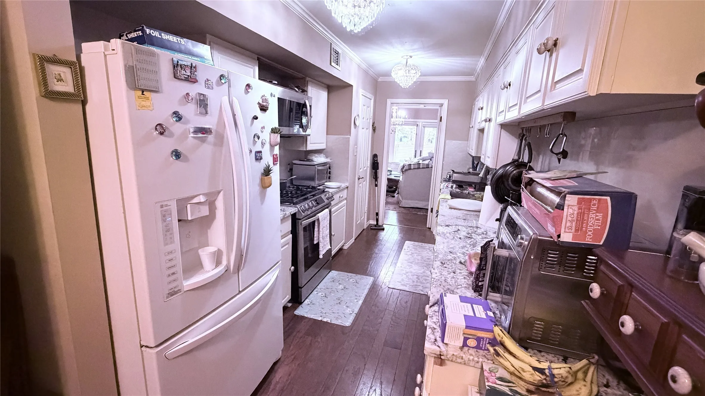 Galley kitchen featuring wood-finish flooring, white cabinetry, integrated appliances, and a chandelier light fixture