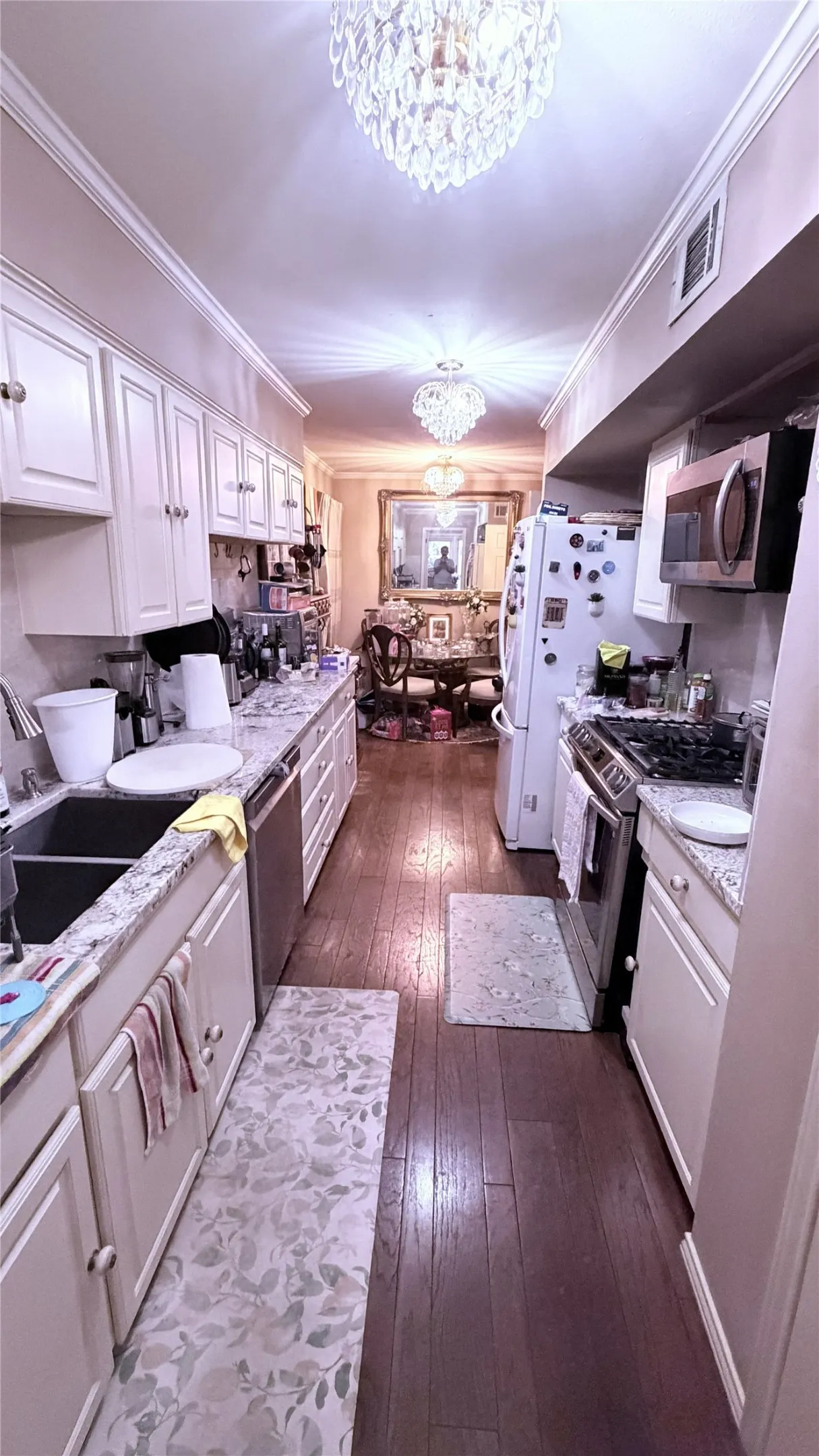 Galley kitchen featuring white cabinetry, stone-finish countertops, stainless steel appliances, and wood-finish flooring