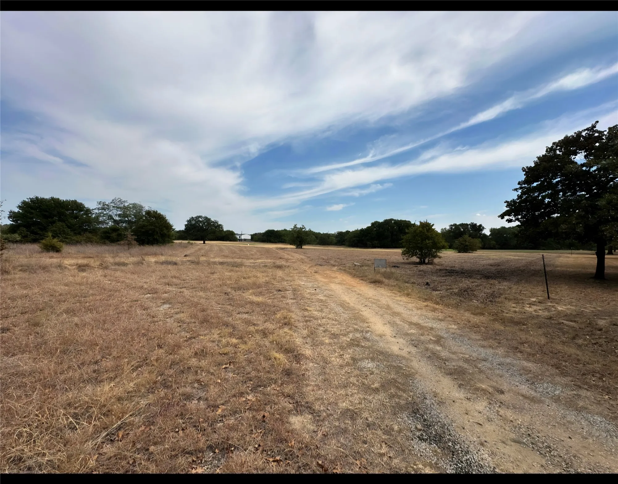 Expansive land parcel featuring a gravel path, mature trees, and natural vegetation