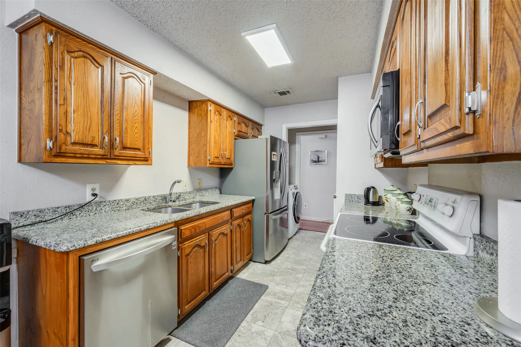 Galley kitchen featuring wood cabinetry, light-toned countertops, a stainless steel dishwasher, and a built-in microwave