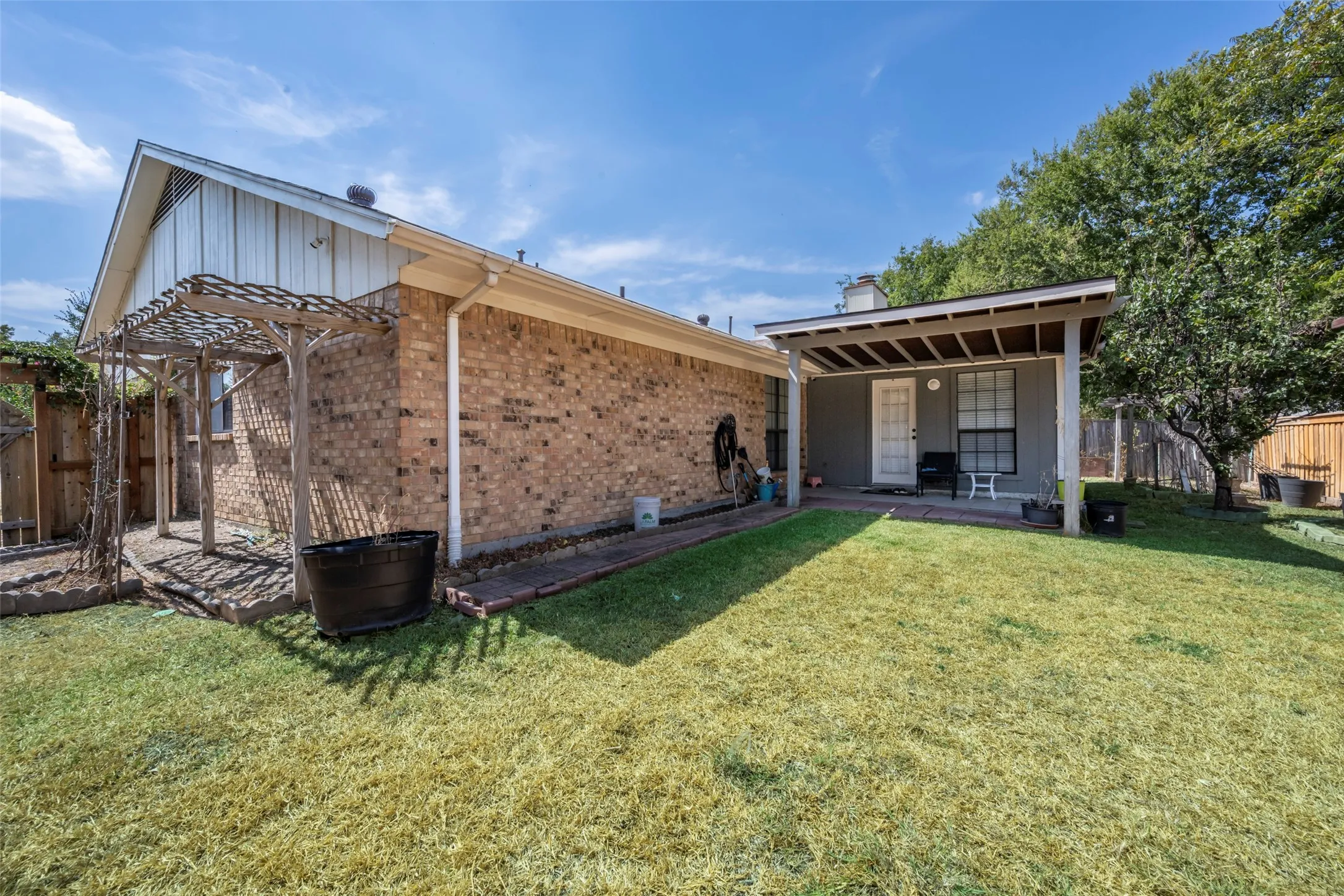 Expansive green lawn, brick exterior, covered patio, pergola structure, and mature perimeter trees