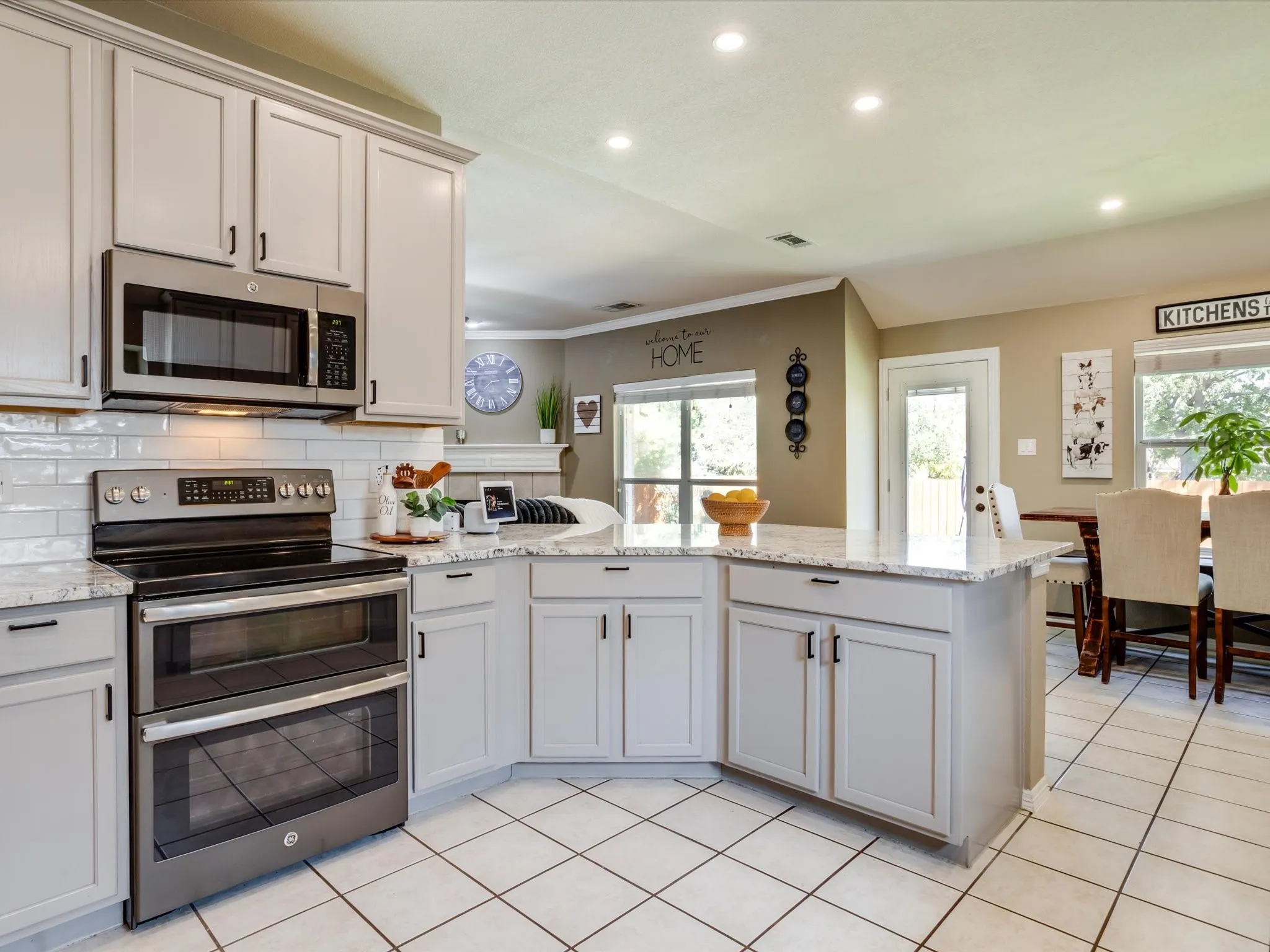 Light-toned cabinetry with dark hardware, stainless steel double oven range, built-in microwave, light-toned countertops, and white tile flooring