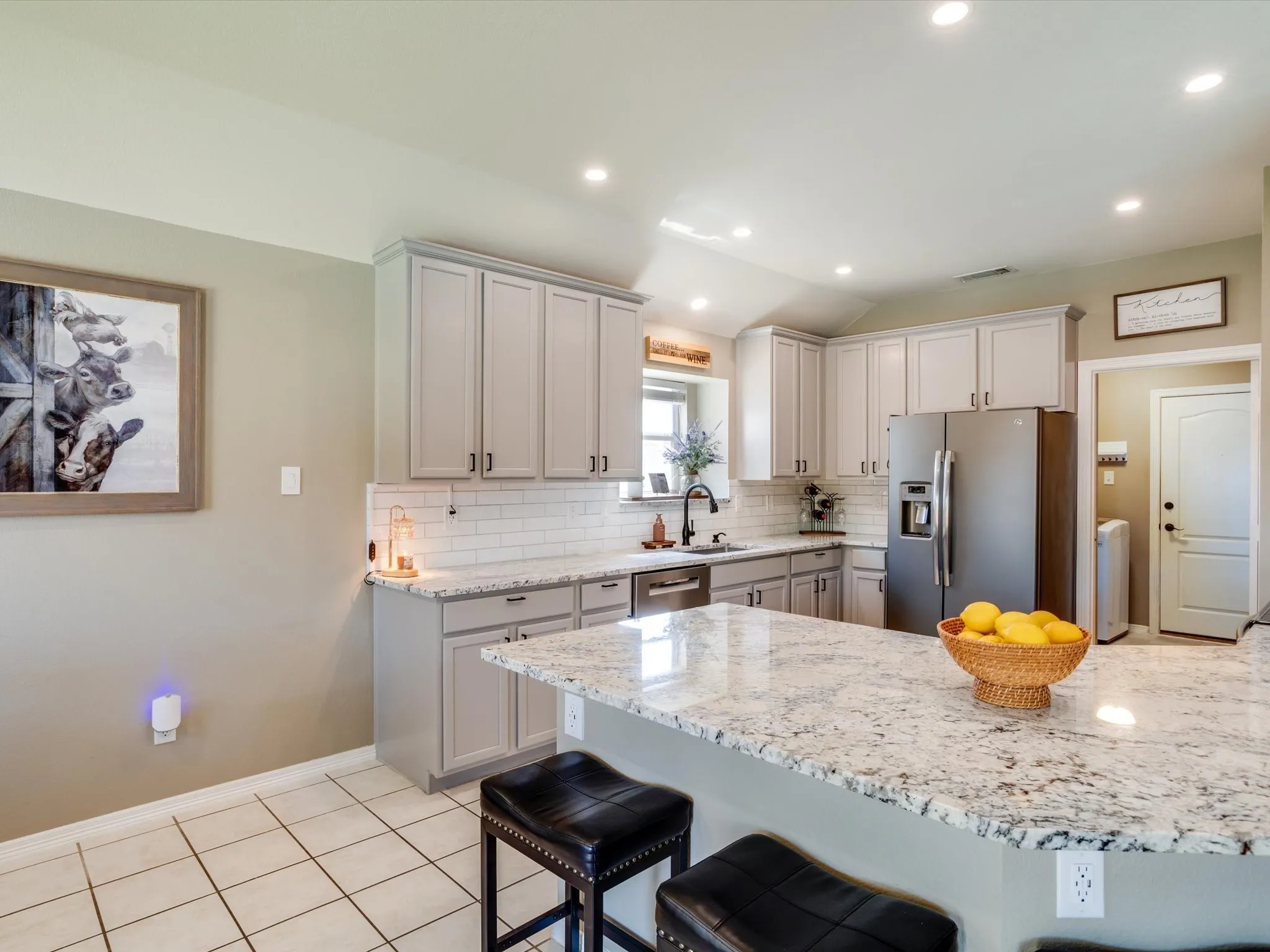 Kitchen with light gray cabinetry, stainless steel appliances, a white subway tile backsplash, and a large island featuring a light-toned countertop