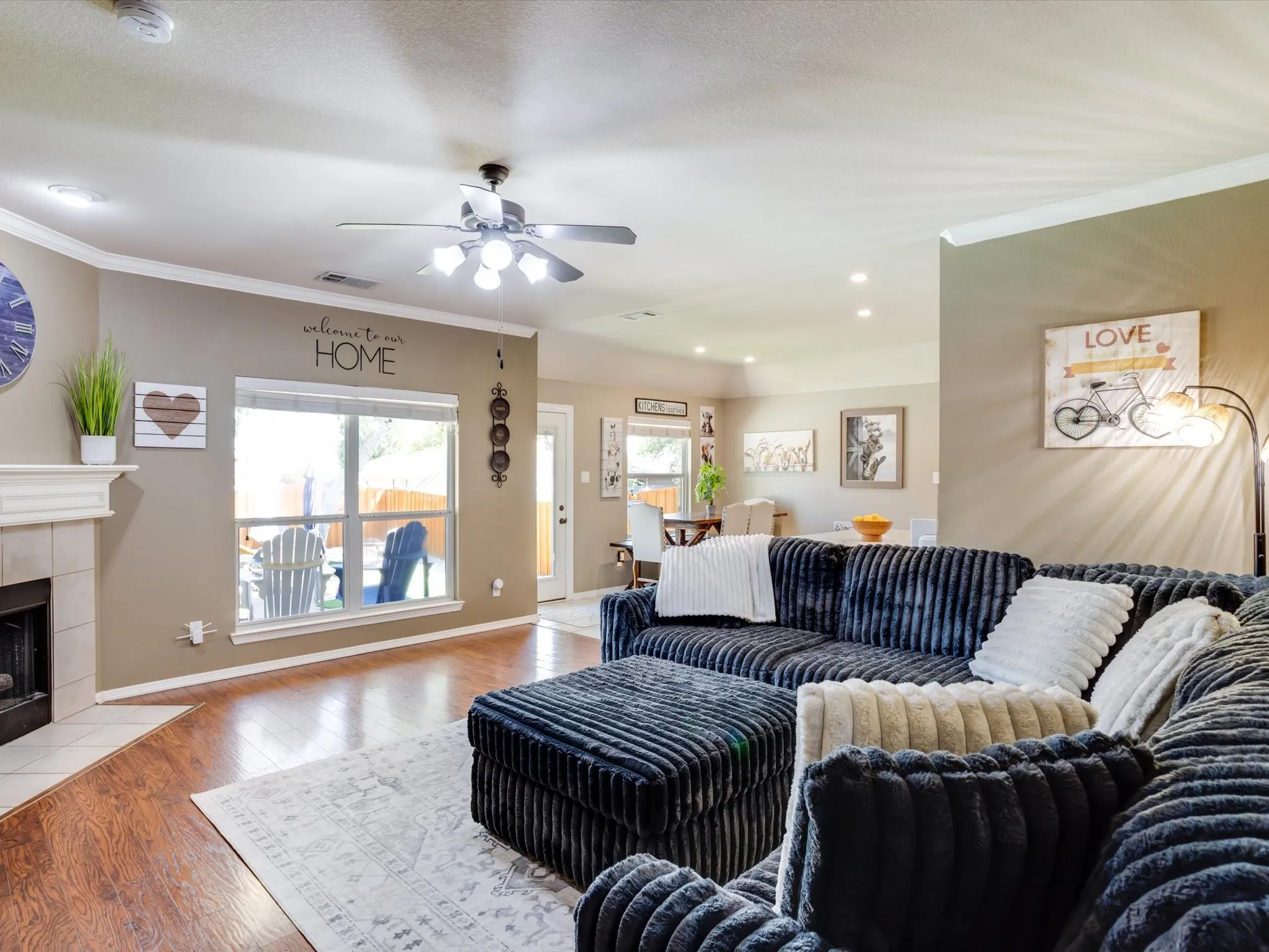 Living area featuring wood-finish flooring, a tiled fireplace with mantel, crown molding, and a ceiling fan