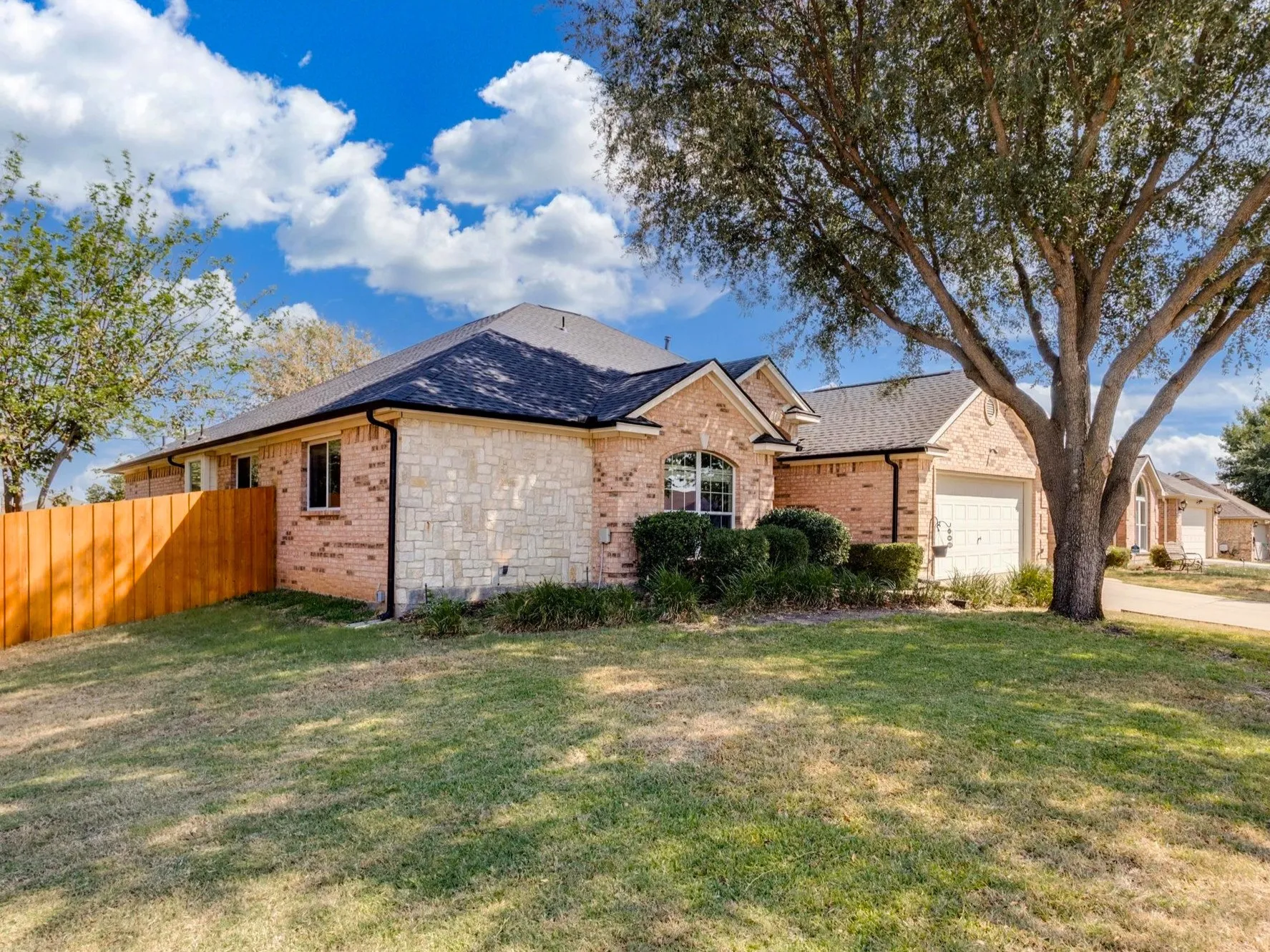 Brick and stone exterior with dark roofing, attached garage, and established landscaping