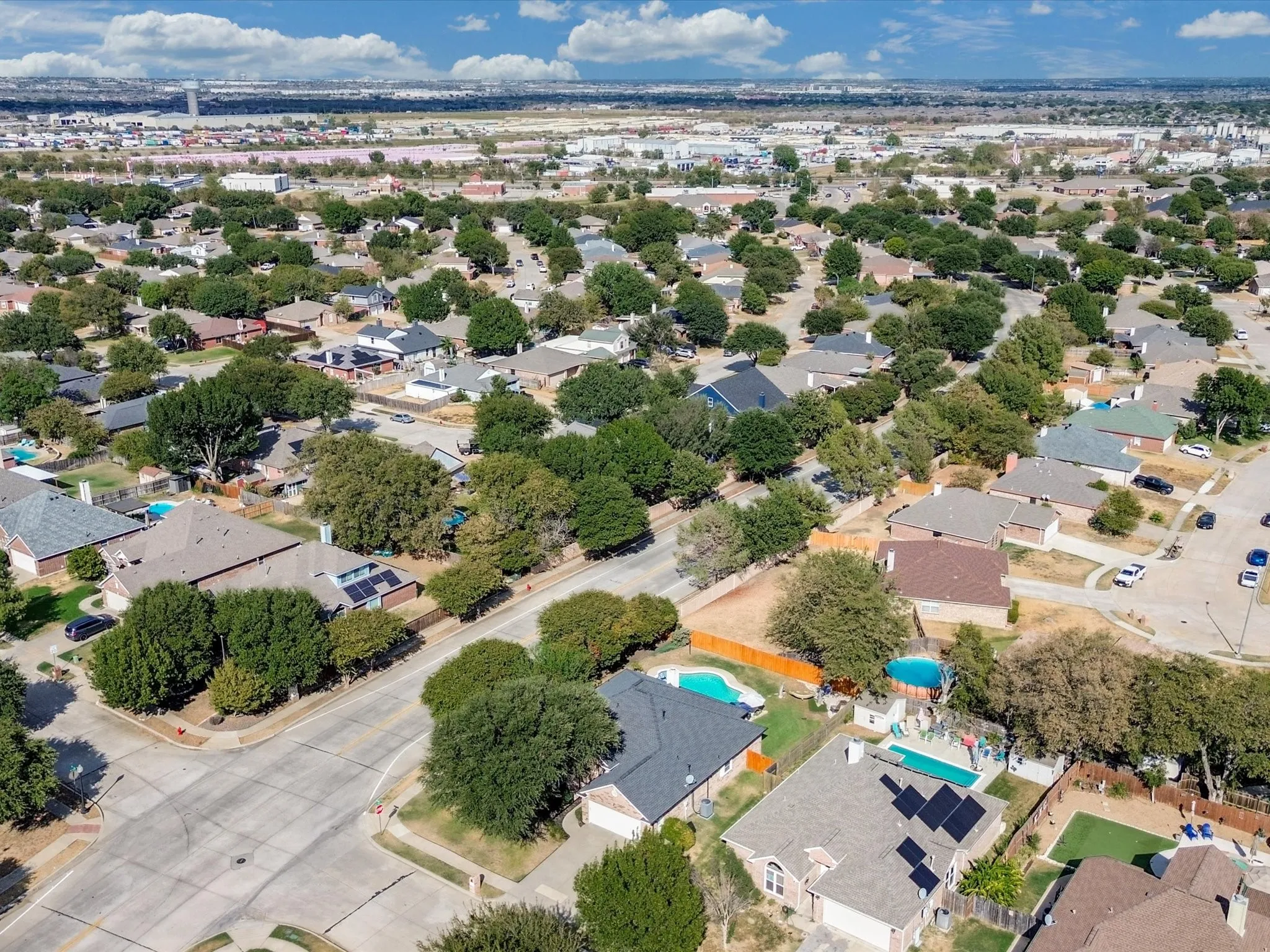 Residential neighborhood with extensive tree canopies, multiple properties featuring swimming pools, and solar panel installations visible on several rooftops