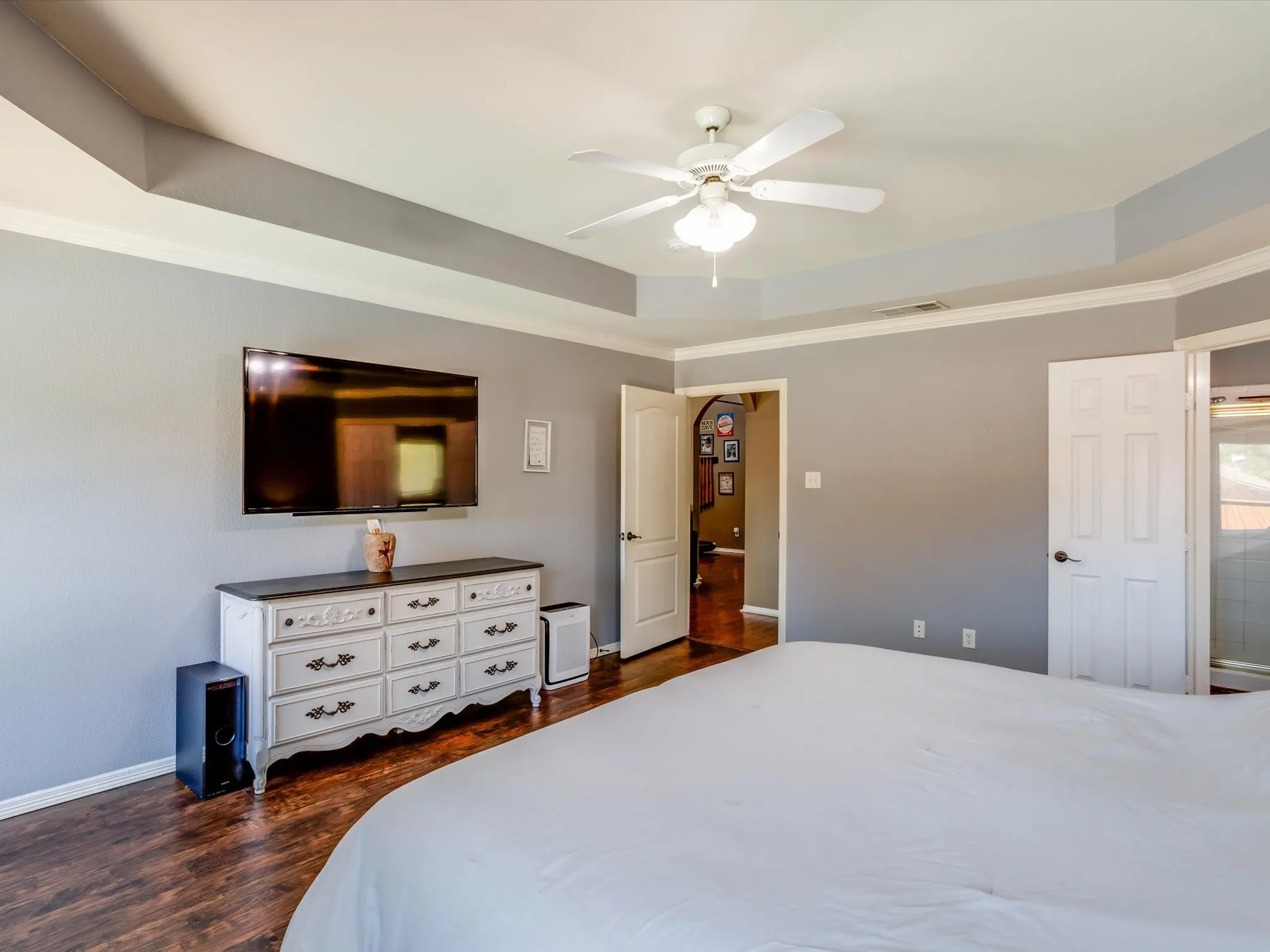Tray ceiling with a ceiling fan, crown molding, wood-finish flooring, and a paneled door