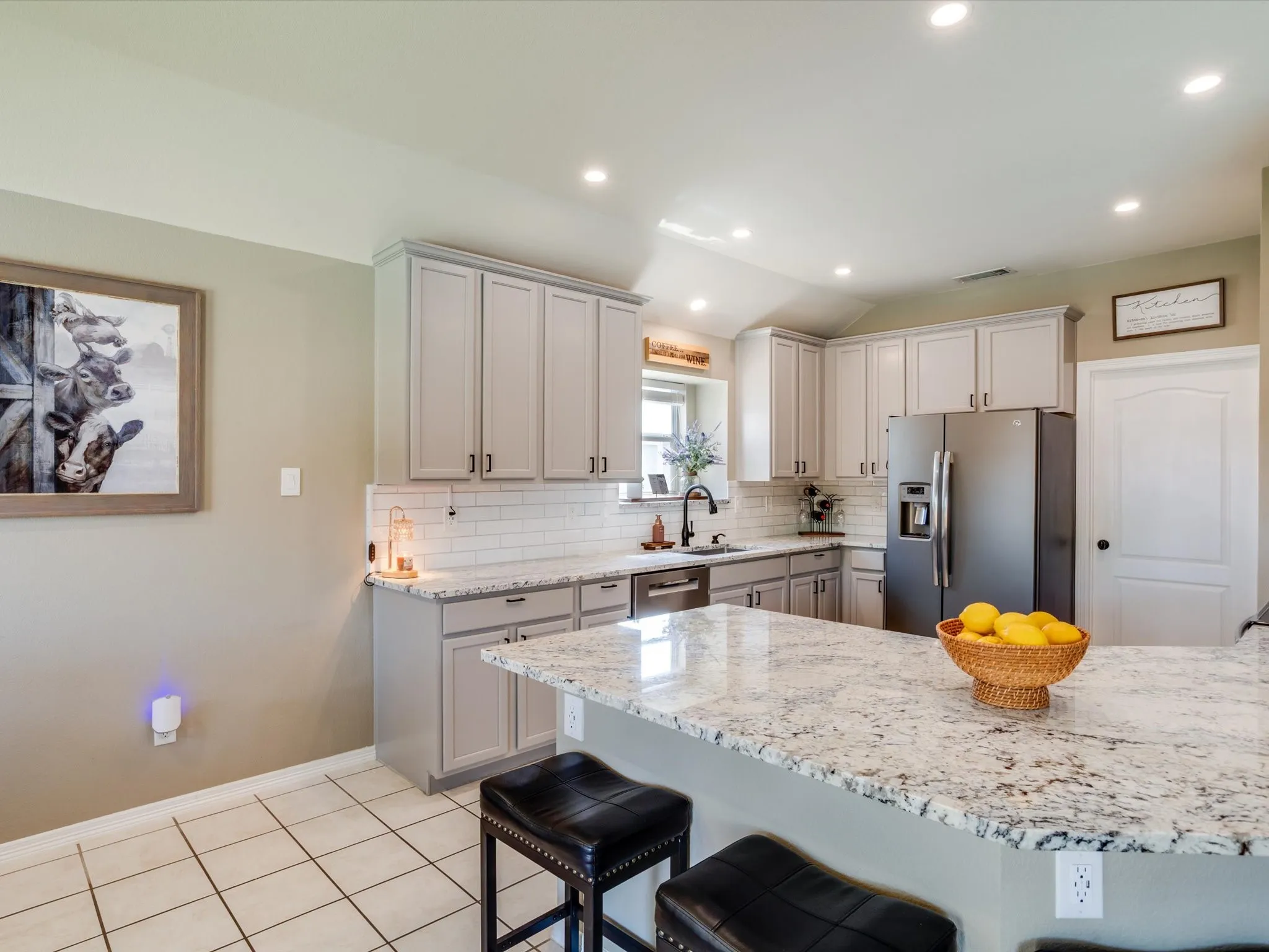 Kitchen featuring light gray cabinetry, white subway tile backsplash, stainless steel appliances, and a central island with a light-toned countertop
