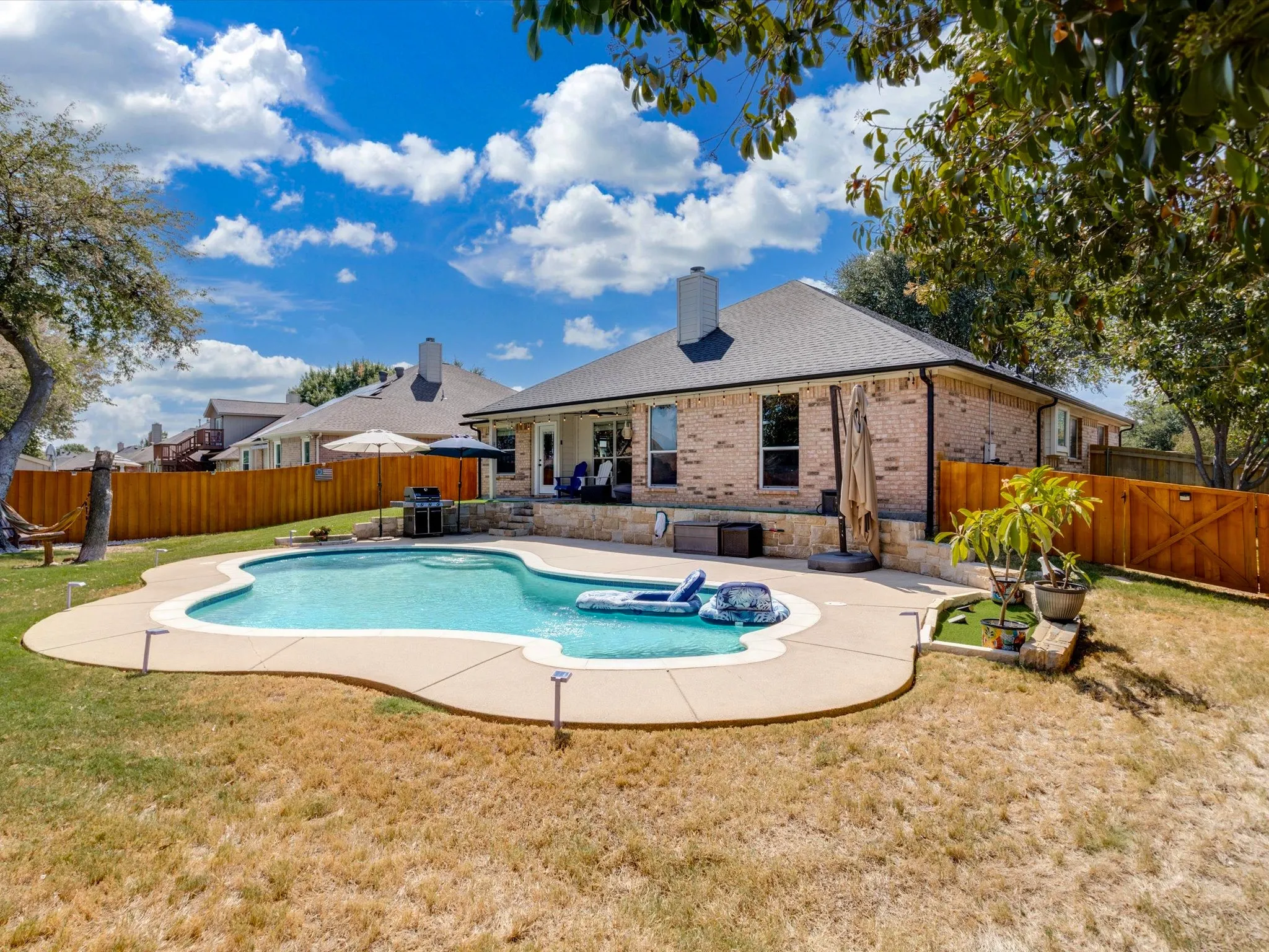 Brick exterior, fenced backyard, in-ground swimming pool, concrete pool deck, and a covered patio area