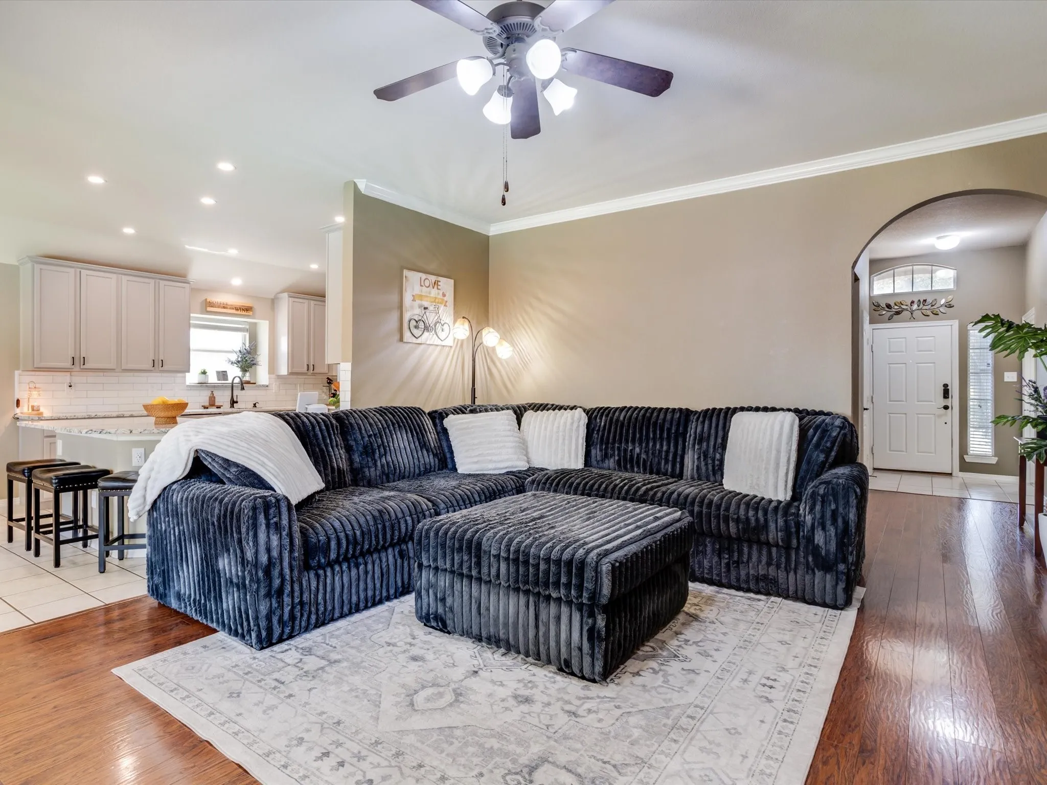 Warm wood-finish flooring, crown molding, and a ceiling fan with integrated lighting