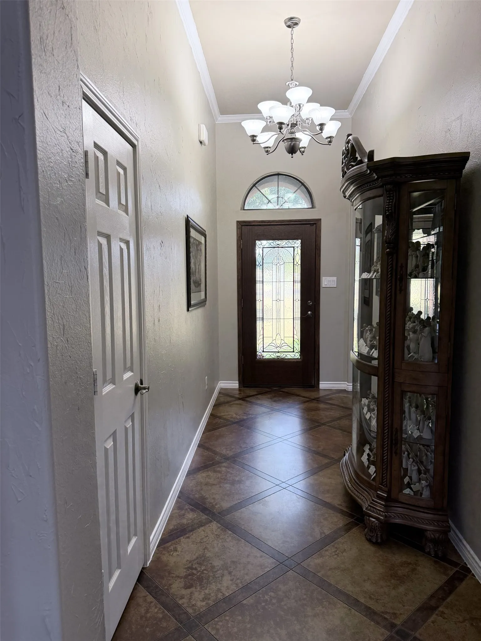 Decorative tiled flooring, crown molding, and a chandelier illuminate the entry