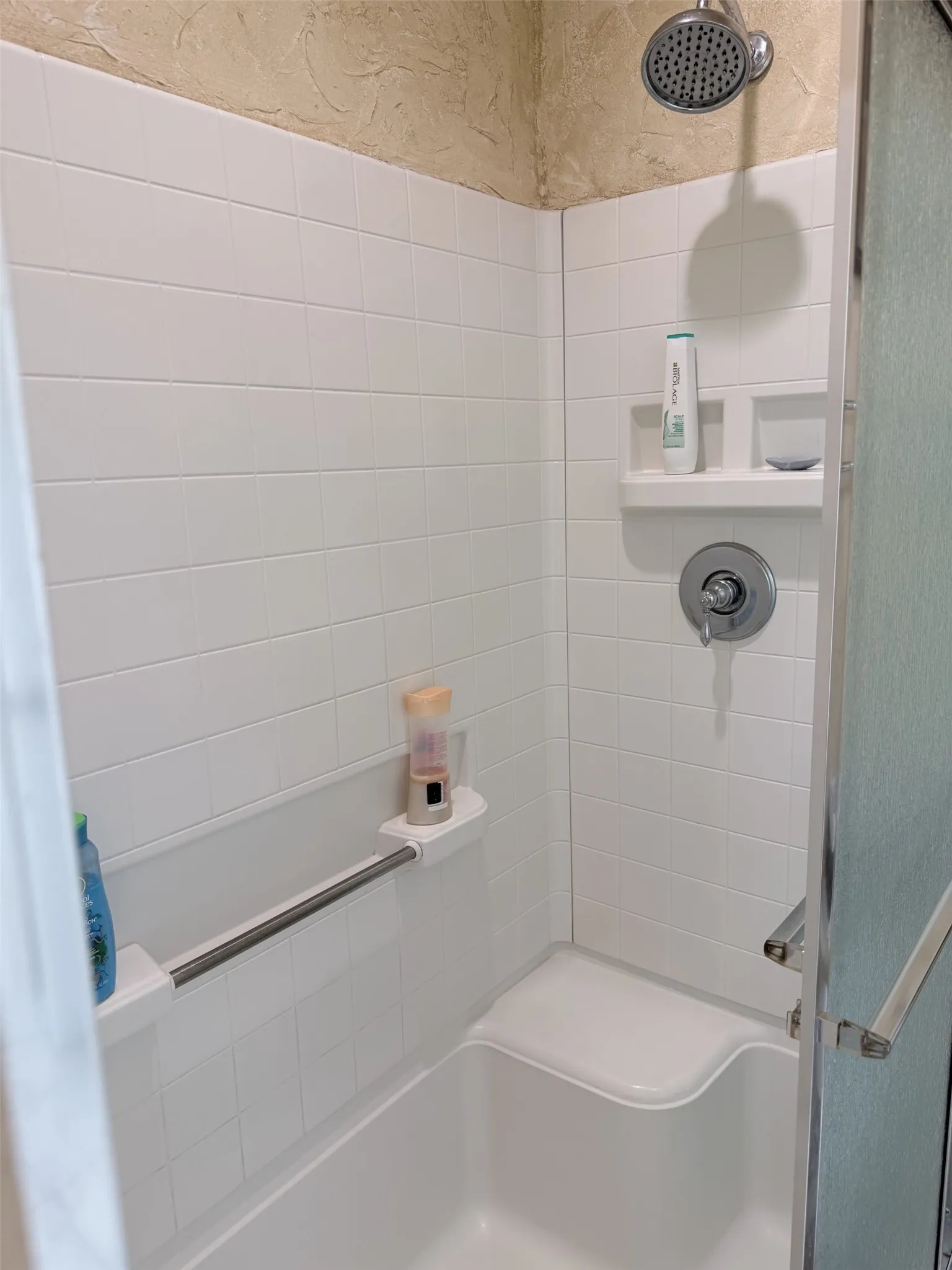 White subway tile surround with textured wall finish, integrated shower seat, and built-in shelving