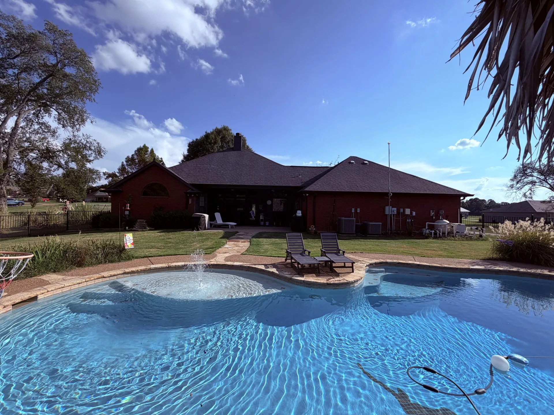Red-sided exterior with a dark shingled roof, featuring a kidney-shaped swimming pool with a water feature, and a stone-paver pathway