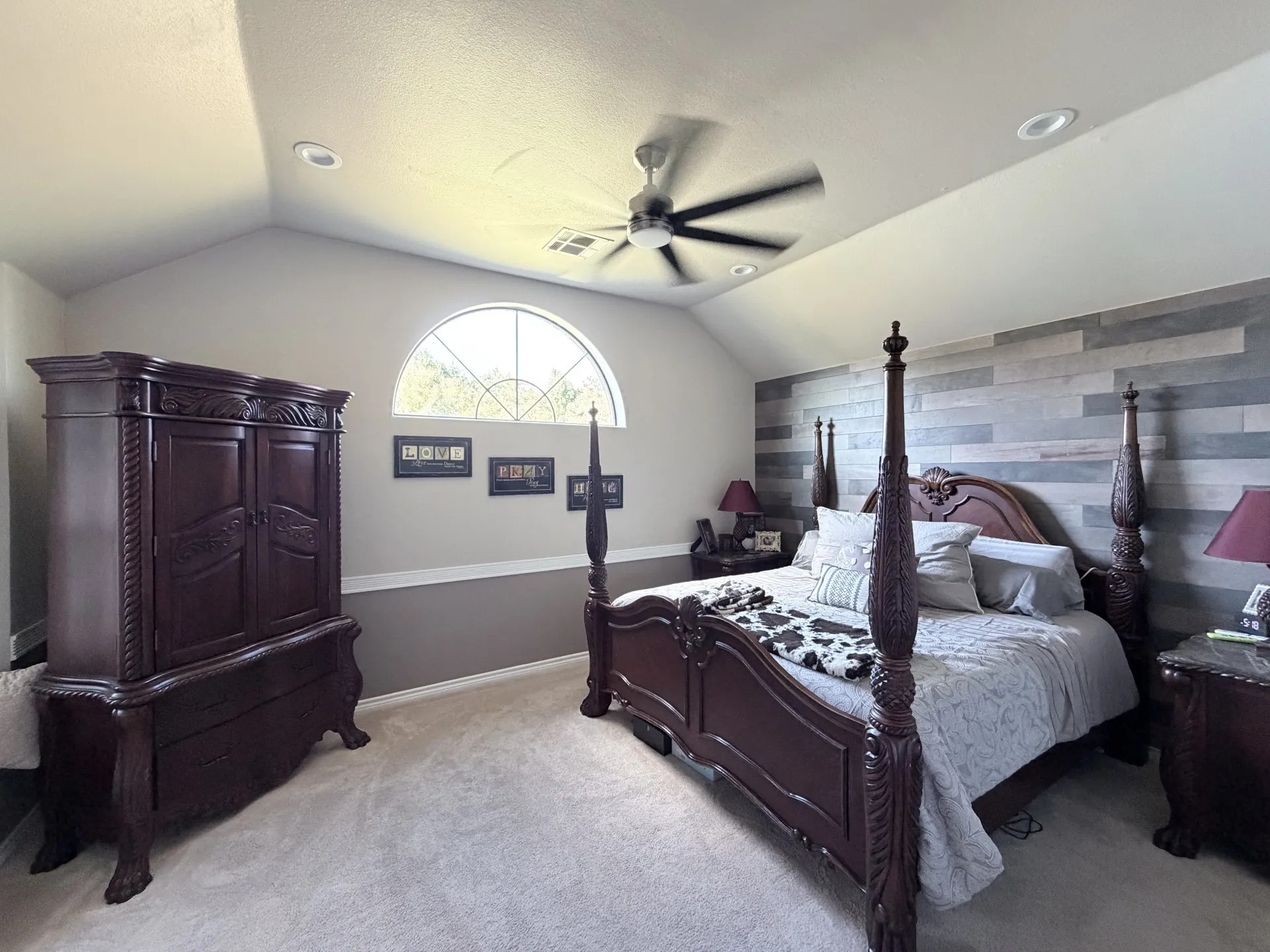 Vaulted ceiling with recessed lighting, ceiling fan, arched window with grid, horizontal wood-finish accent wall, and carpeting