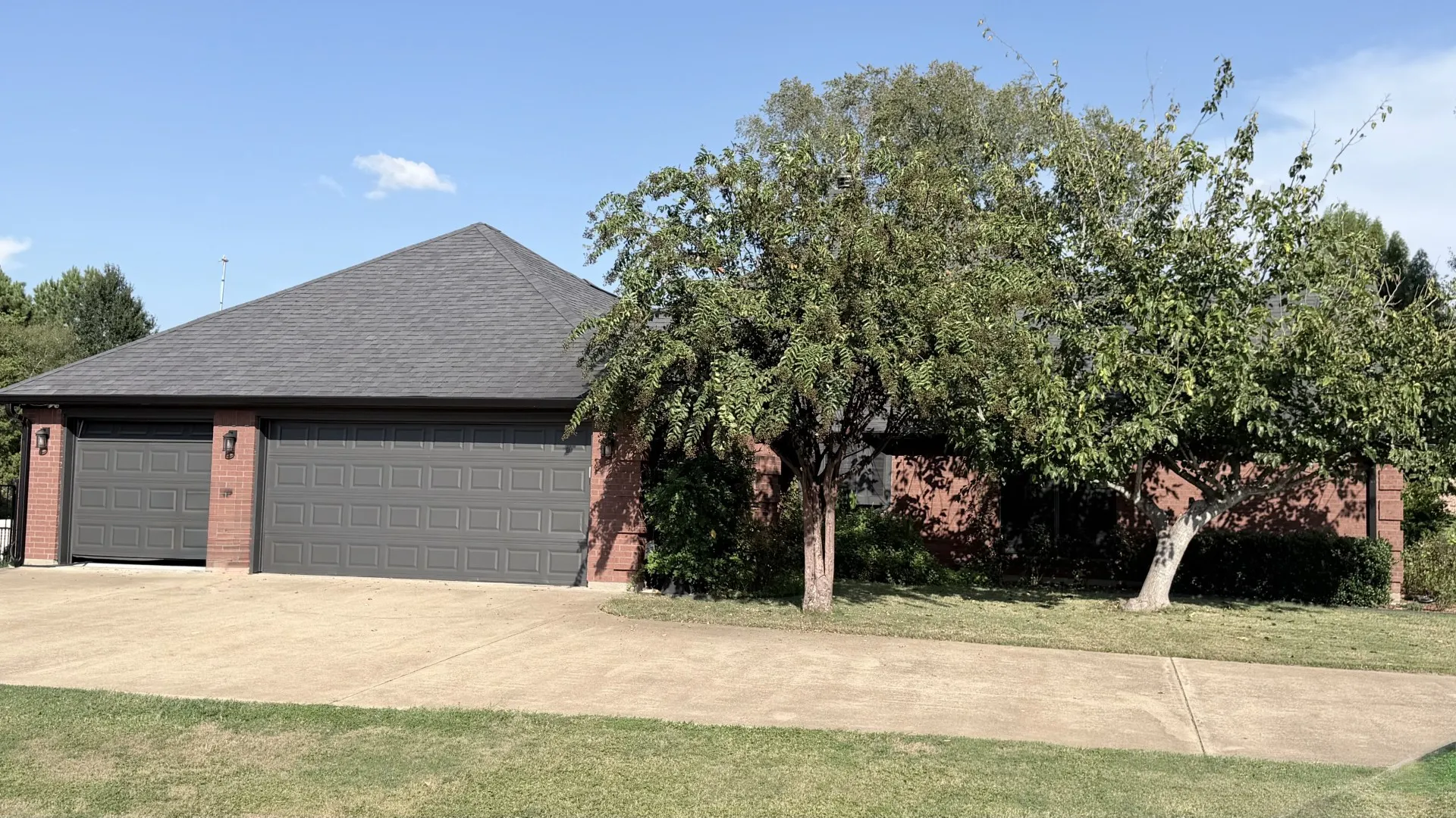 Brick exterior with a dark shingle roof, double garage doors, and mature trees