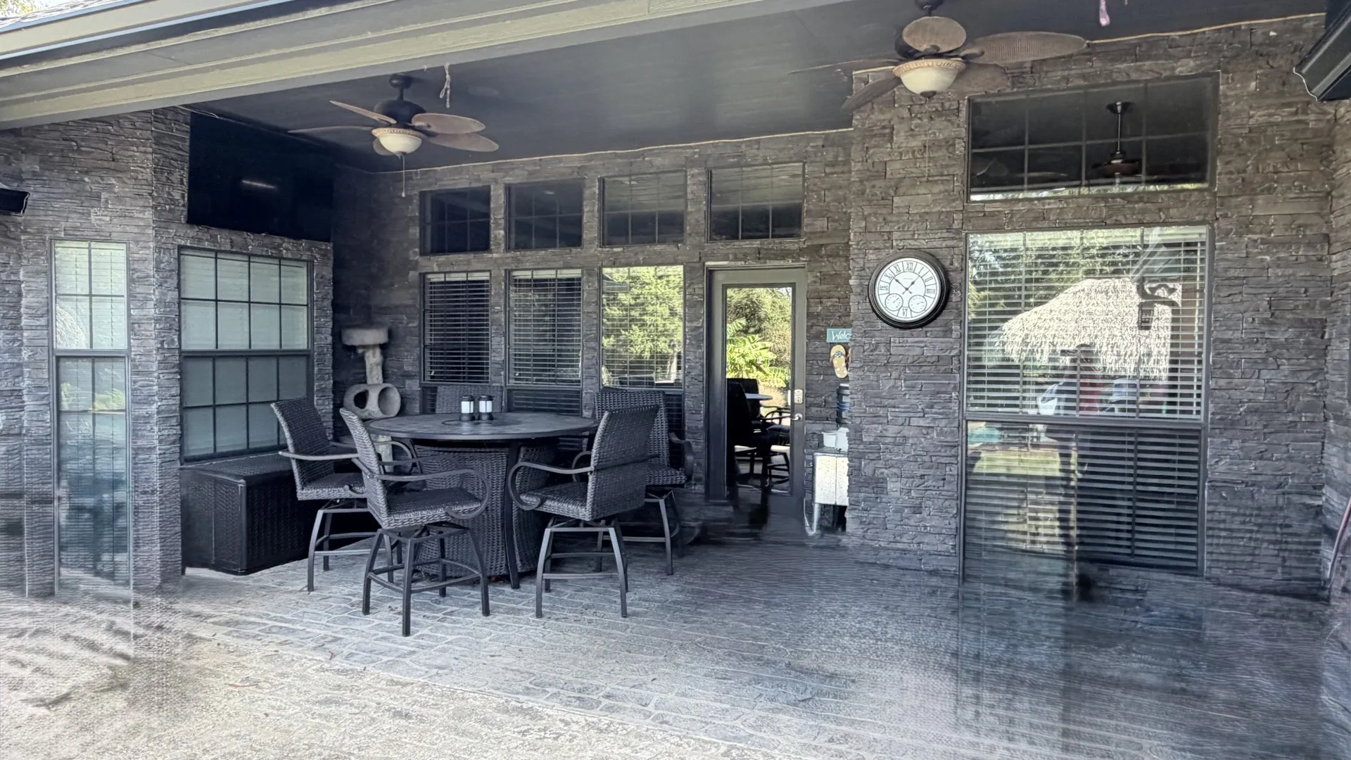 Expansive covered patio featuring stone-clad walls, multiple windows, and dual ceiling fans