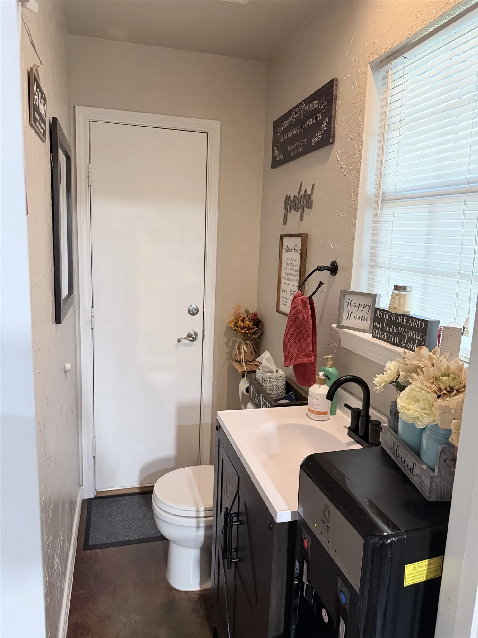 Window with blinds, integrated sink and countertop, dark wood-finish vanity with cabinet storage, contemporary black faucet, and white toilet