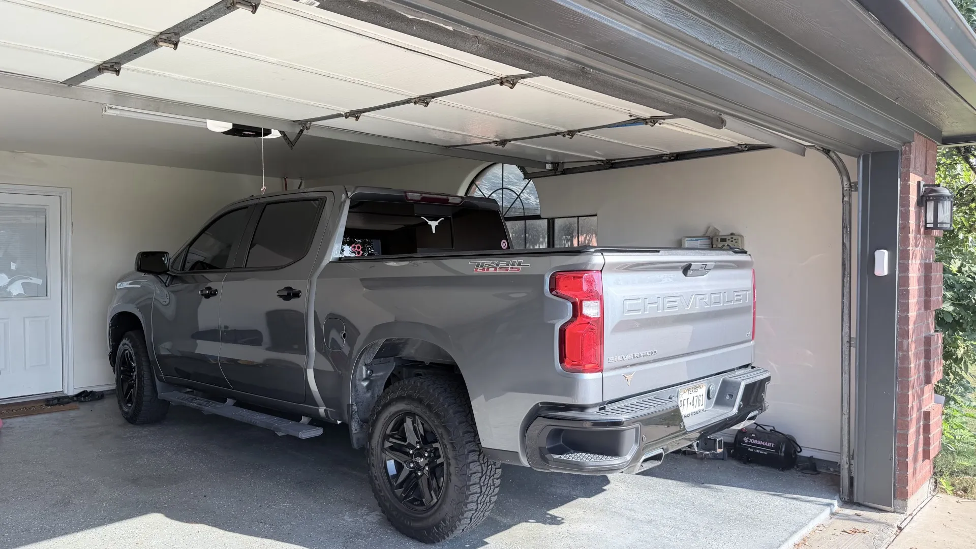 Garage with an automatic overhead door opener, interior access door, and exterior brick column with a mounted light fixture
