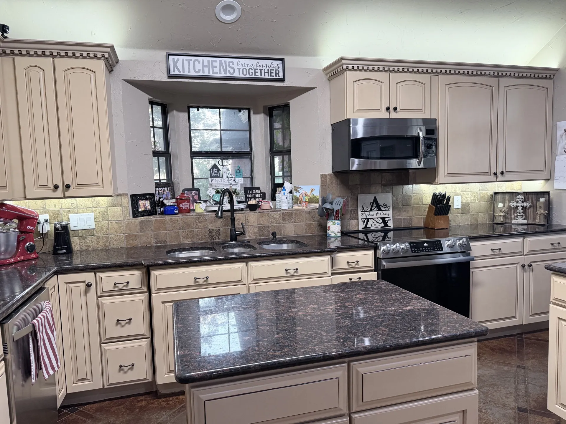 Kitchen featuring an island, light-toned cabinetry, dark countertops, built-in microwave, and a double basin sink