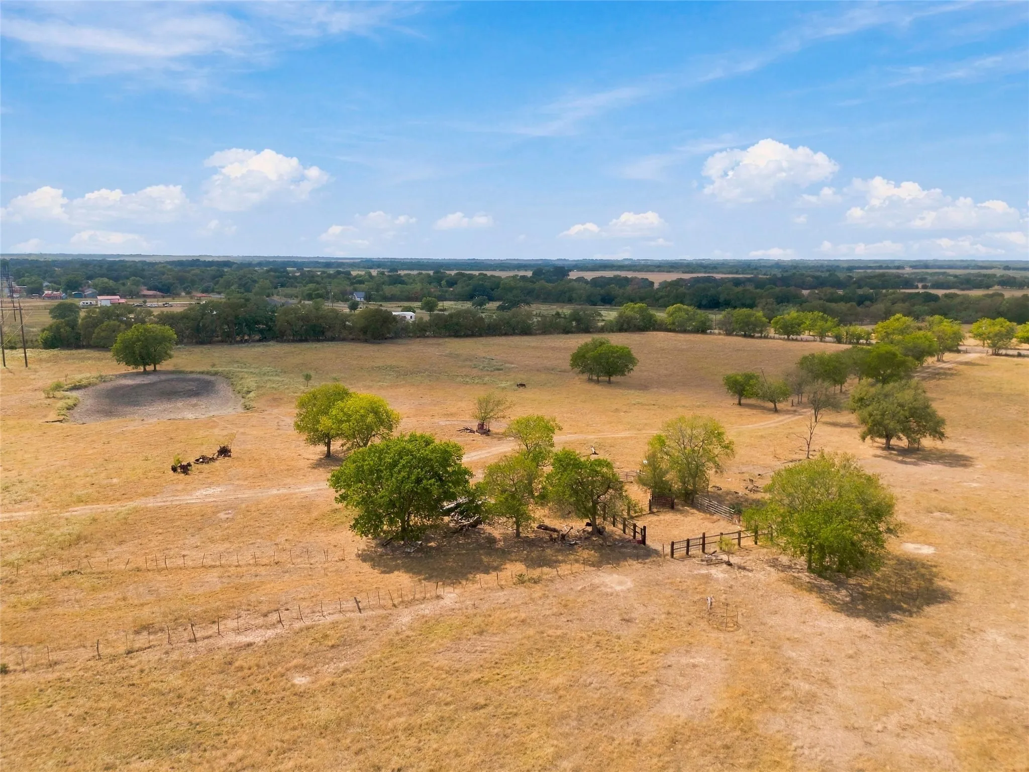 Expansive rural landscape featuring scattered trees, a natural pond, and perimeter fencing