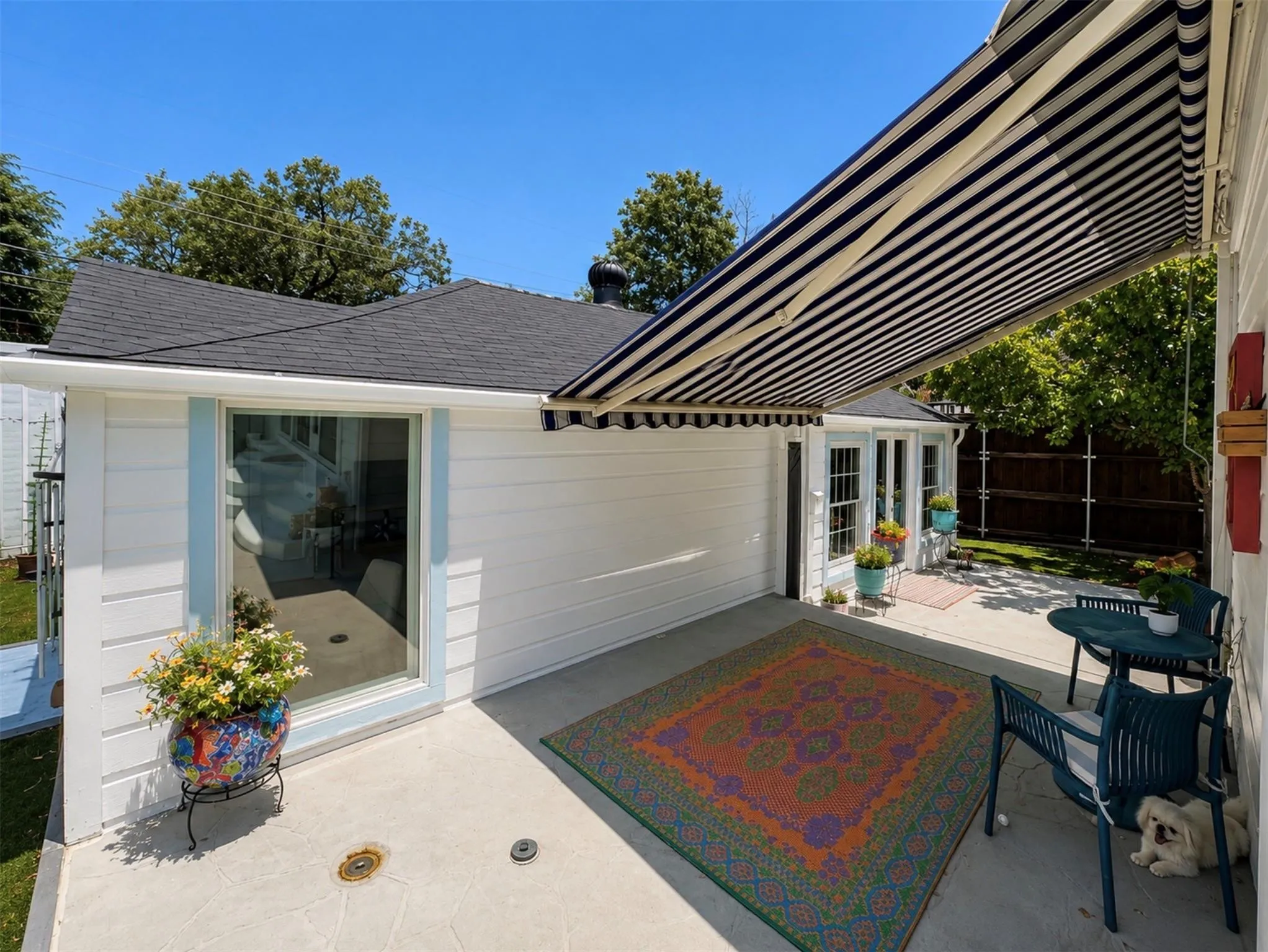 Paved patio with an extendable striped awning, exterior siding, and a gabled roof