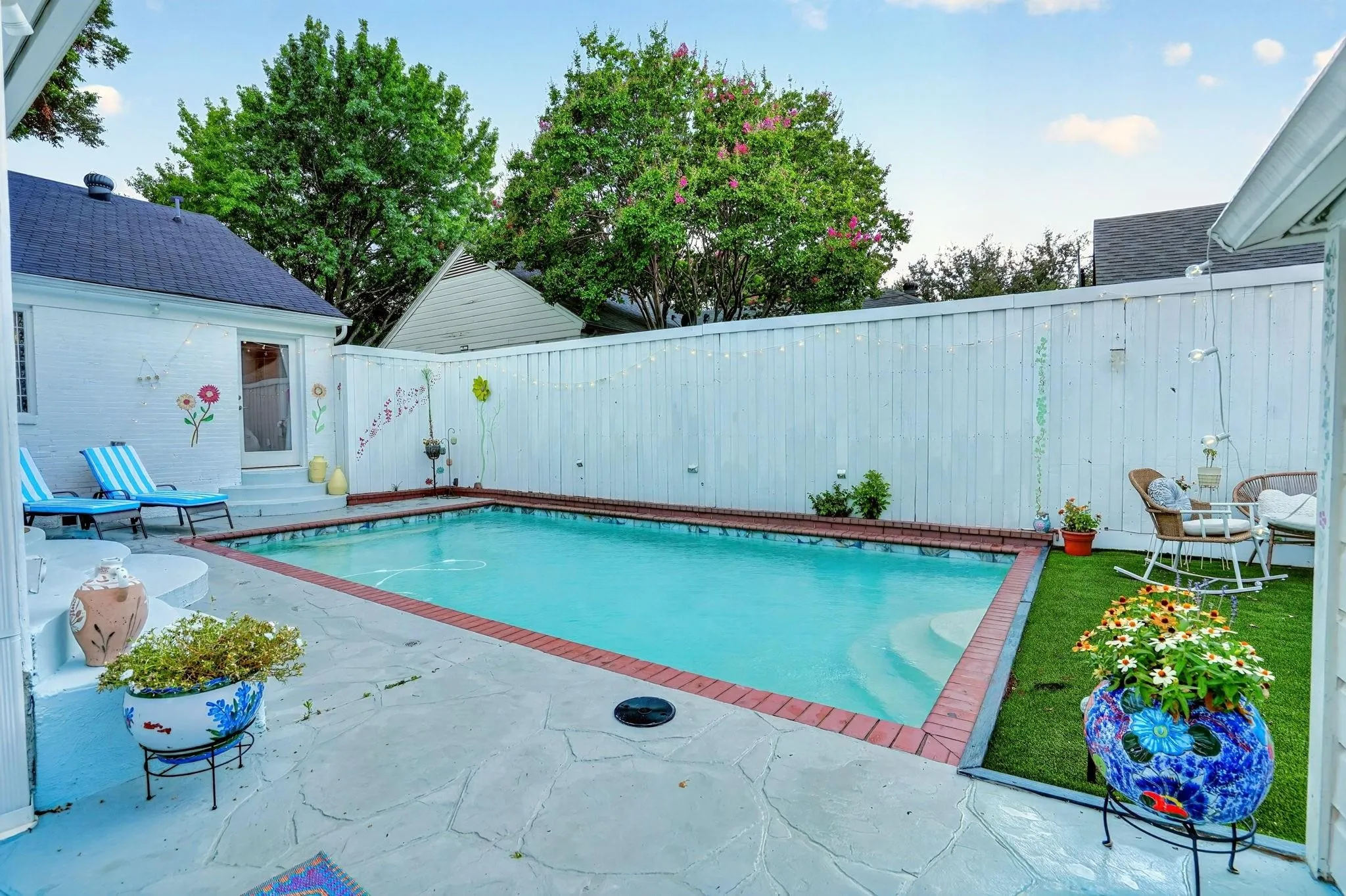 Private backyard pool with brick coping, stone patio, and artificial turf area