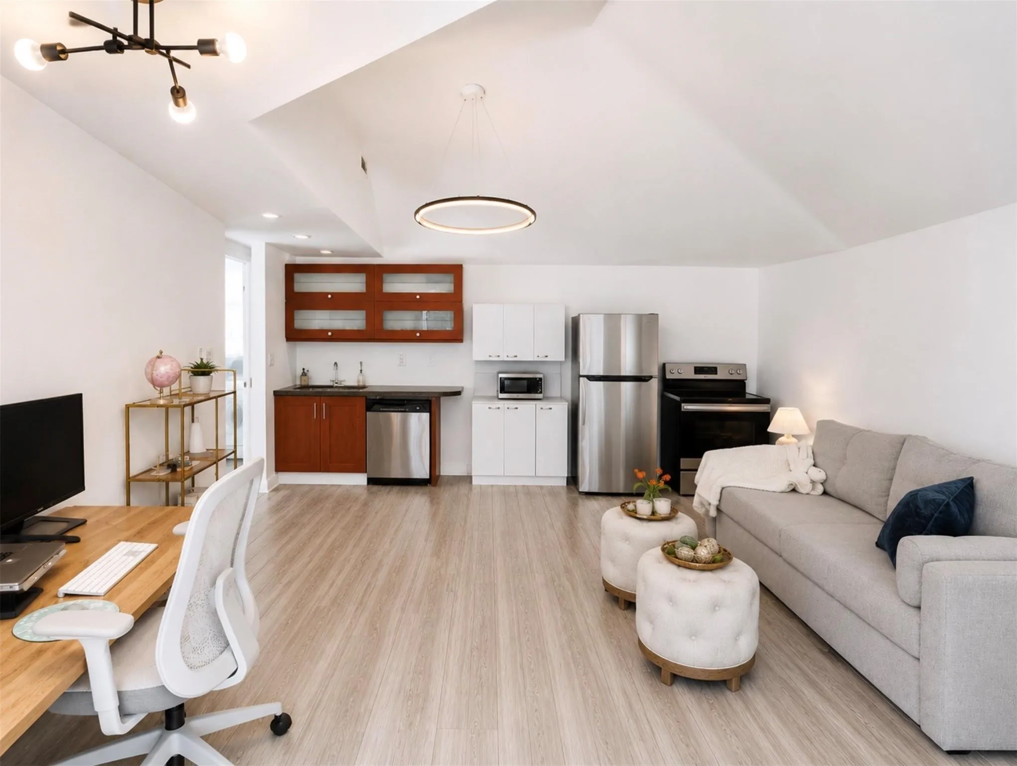 Vaulted ceiling with modern lighting fixtures, wood-finish flooring, built-in wet bar with glass-front cabinetry, stainless steel appliances, and a built-in workstation