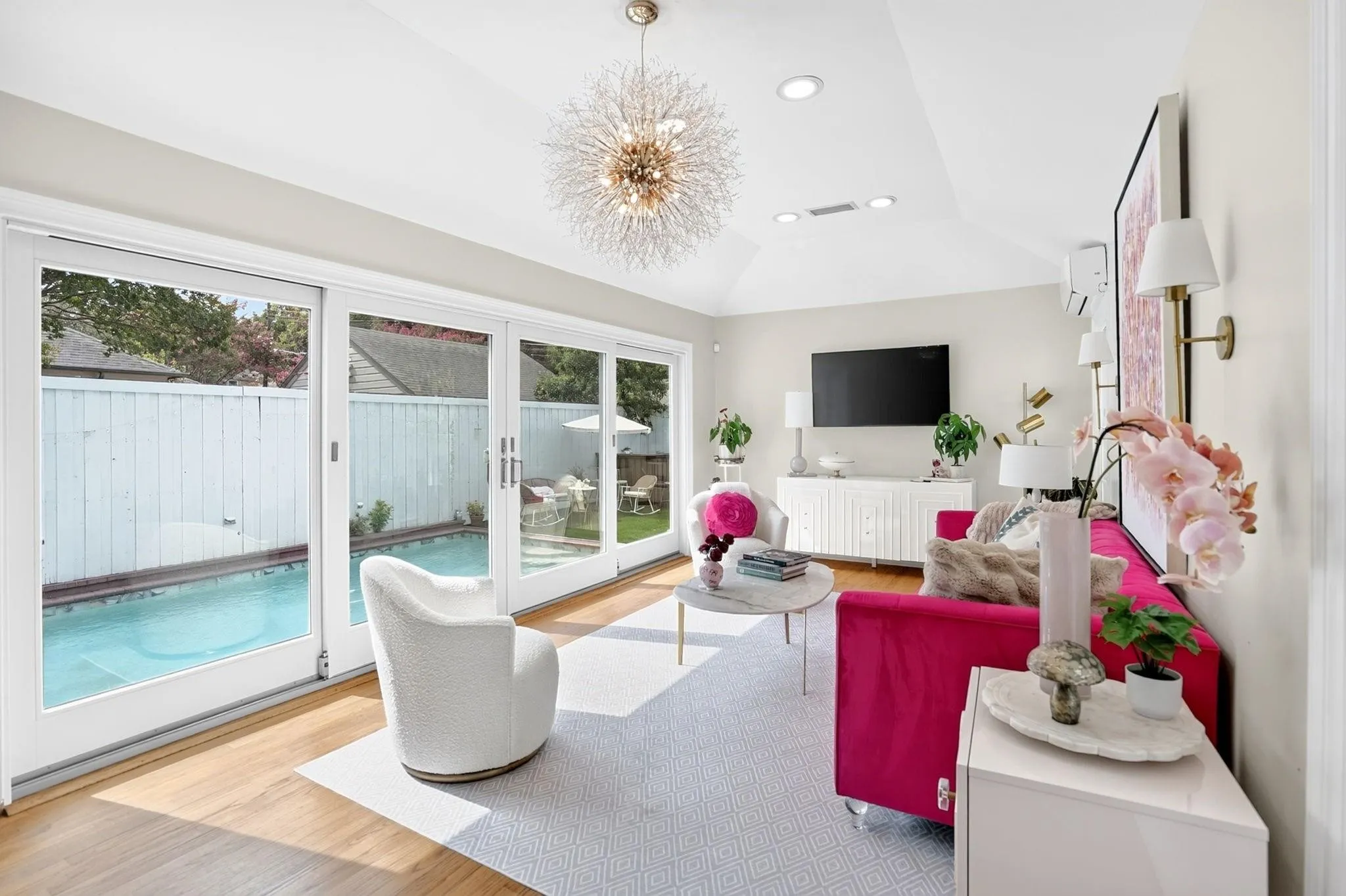Vaulted ceiling with recessed lighting, wood-finish flooring, sliding glass doors to outdoor pool, and a contemporary chandelier