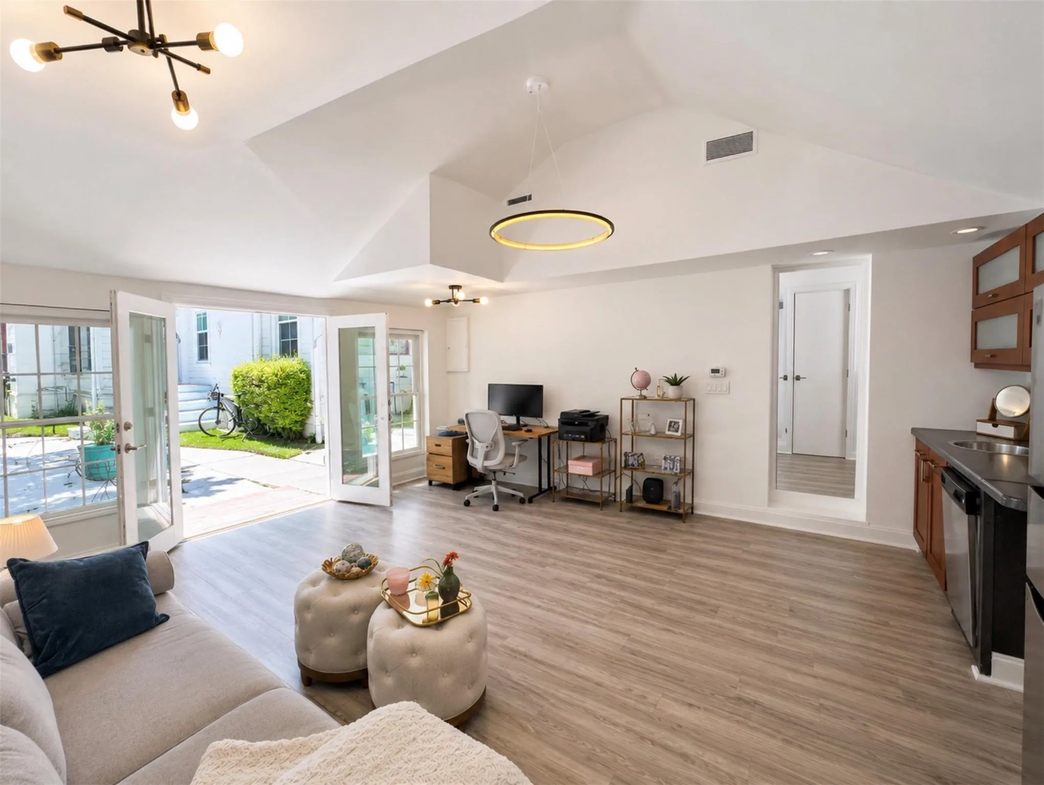 Vaulted ceilings, wood-finish flooring, and multiple sets of French doors opening to an exterior patio