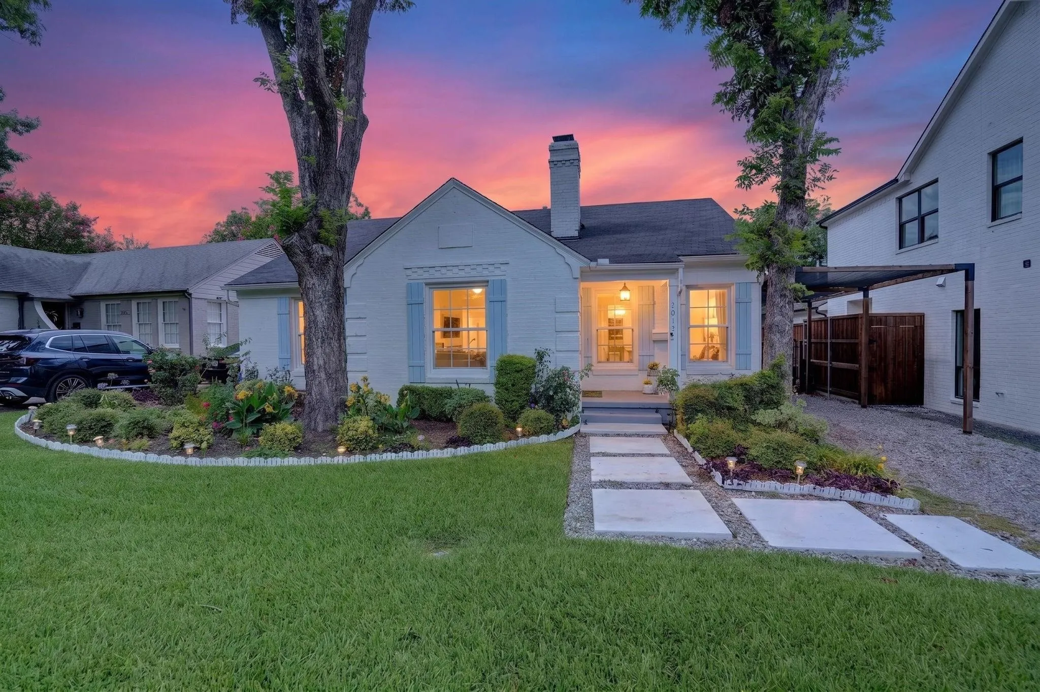 White painted brick exterior with light blue shutters, a front entry porch, and a gravel driveway with a carport