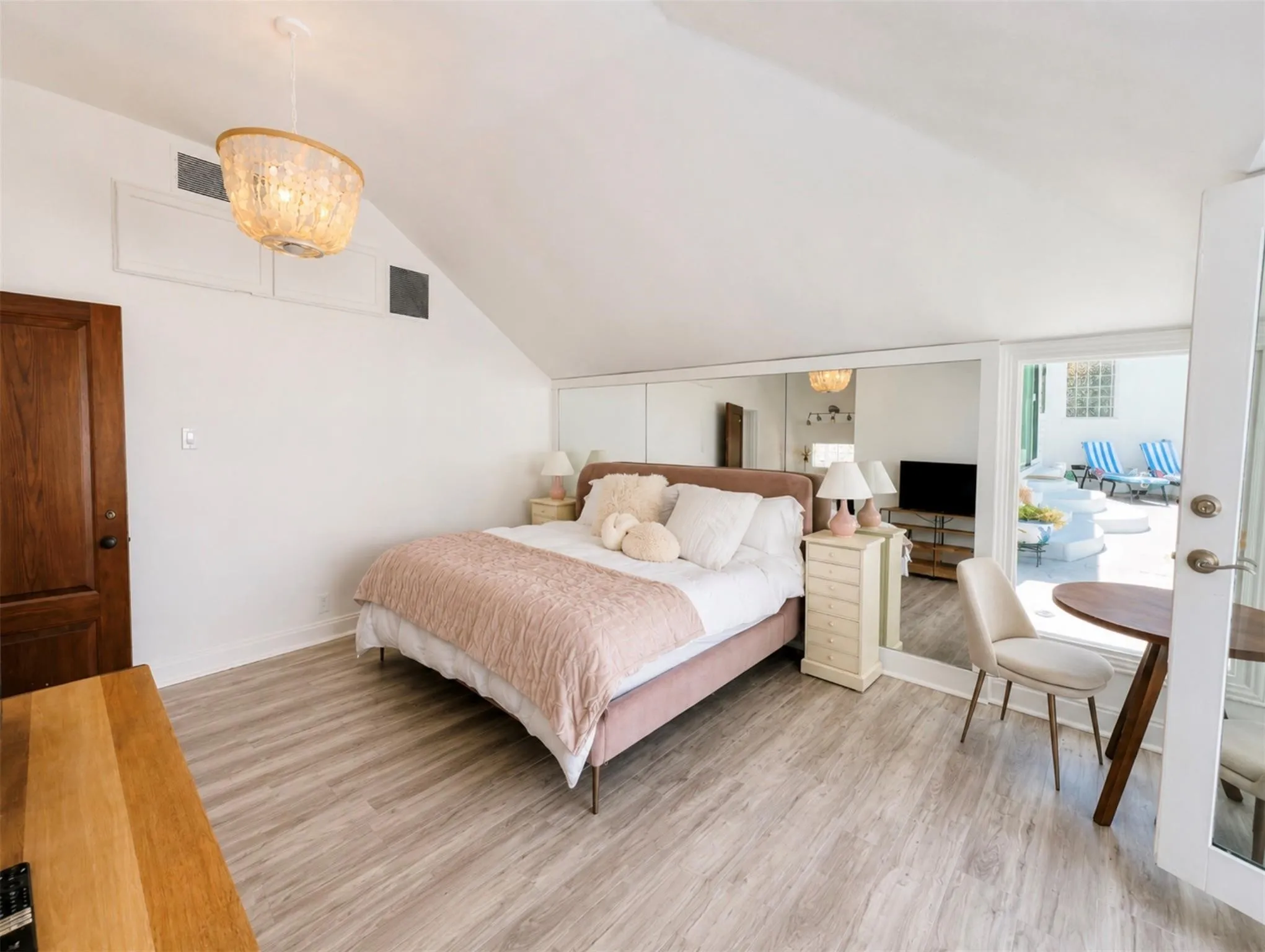 Sloped ceiling room featuring light wood-finish flooring, a wood panel door, and mirrored wall panels