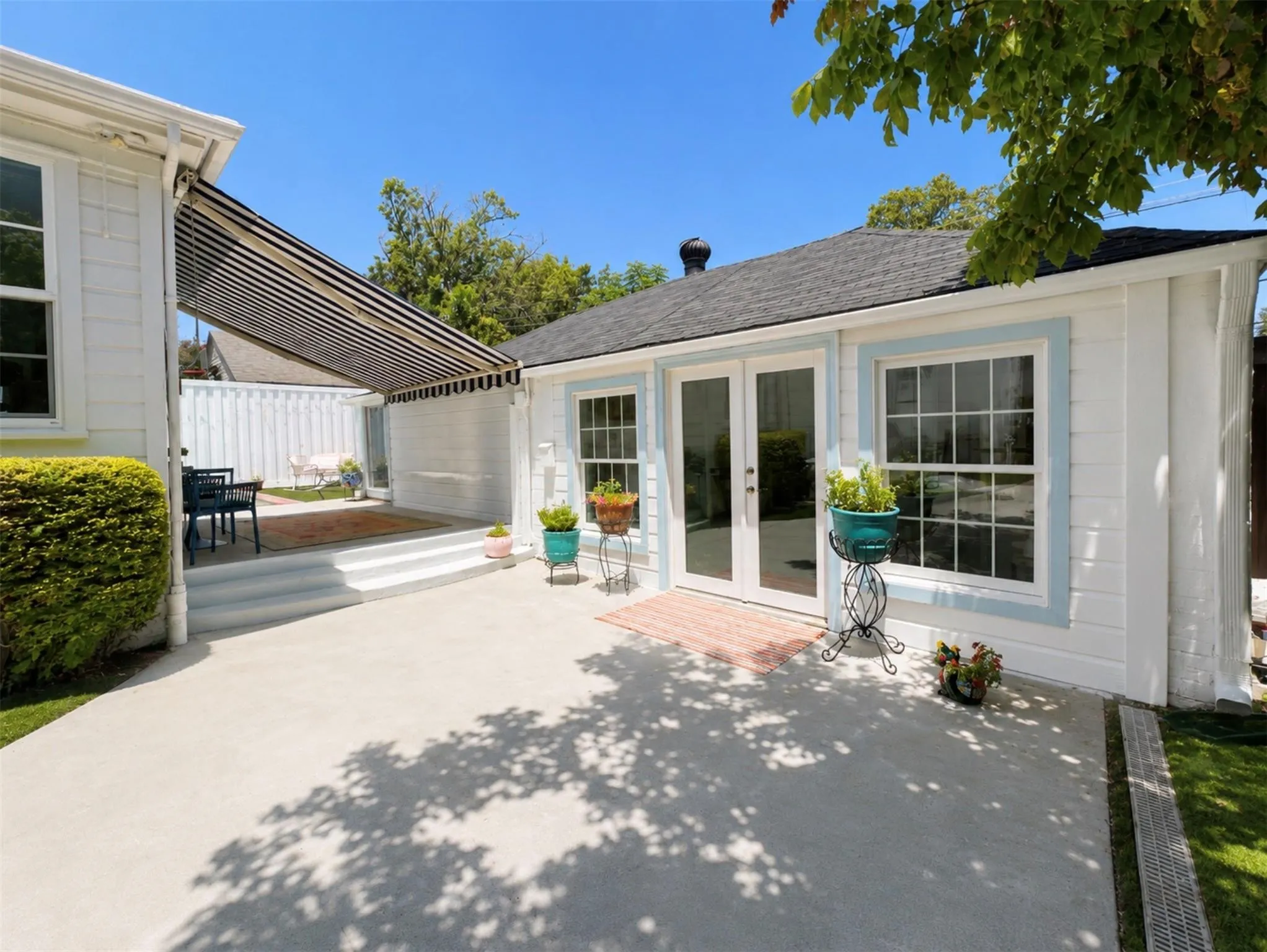 Expansive concrete patio, multi-level patio with steps, retractable striped awning, double French doors, and a shingled roof