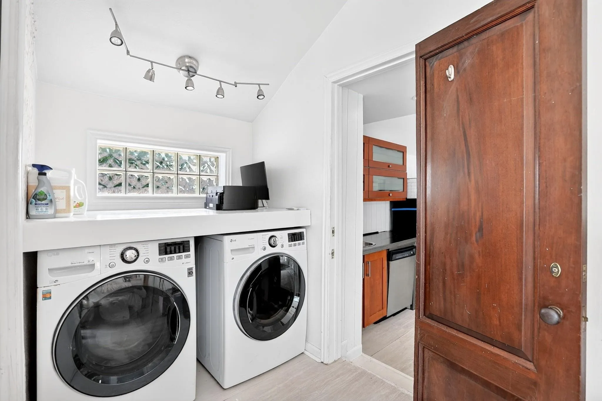Dedicated laundry area with a built-in counter, front-loading washer and dryer, and a glass block window