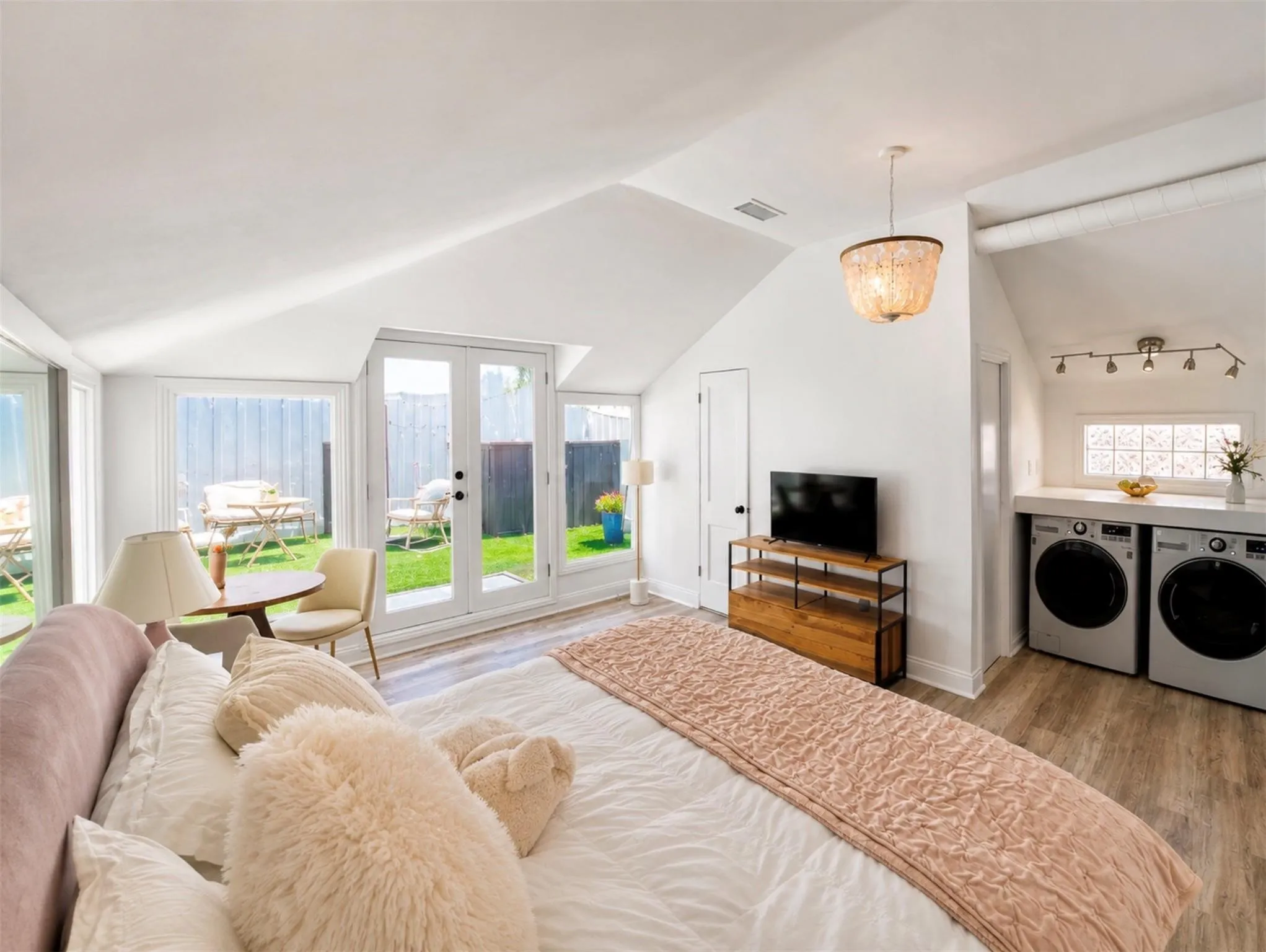 Vaulted ceiling with a chandelier, wood-finish flooring, white French doors, and built-in laundry appliances with a countertop