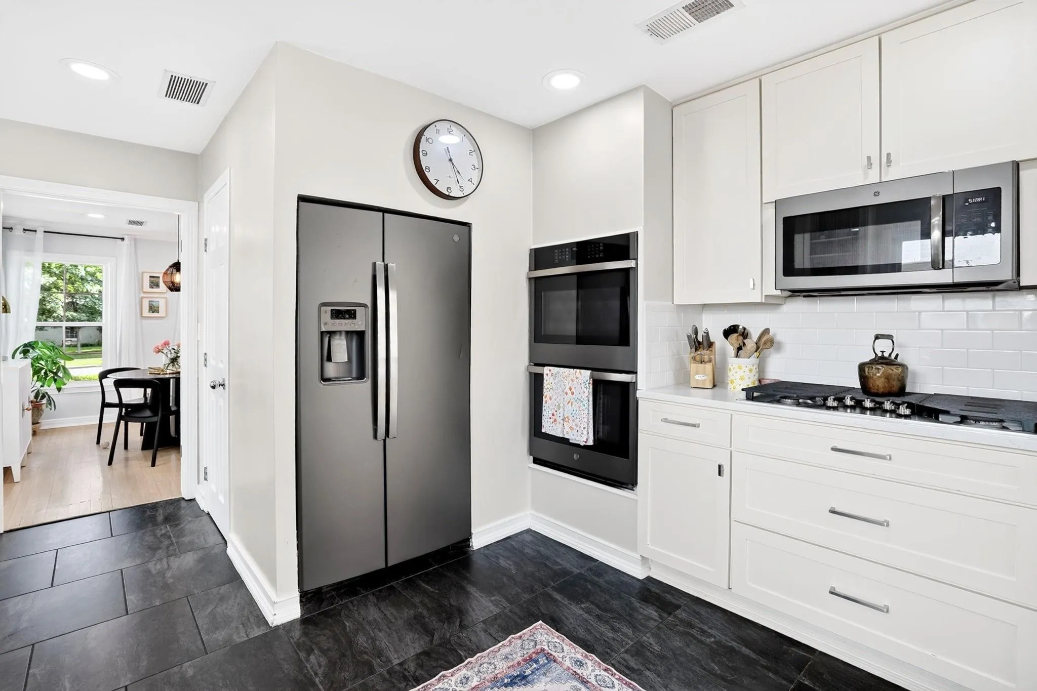 Kitchen featuring dark tile flooring, white shaker cabinets, stainless steel appliances, white subway tile backsplash, and recessed lighting