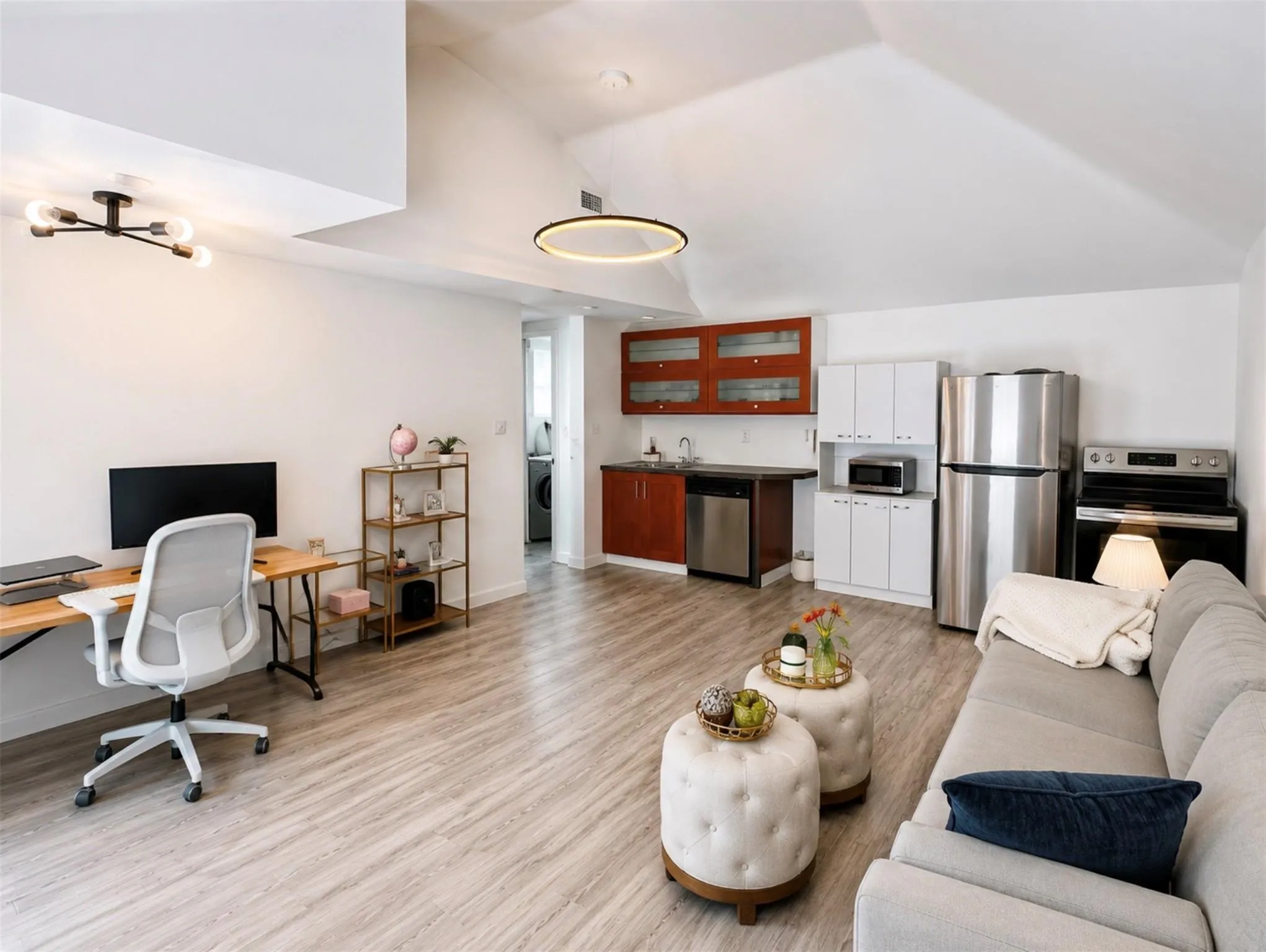 Open-concept living area featuring wood-finish flooring, a kitchen with stainless steel appliances, and a dedicated workspace