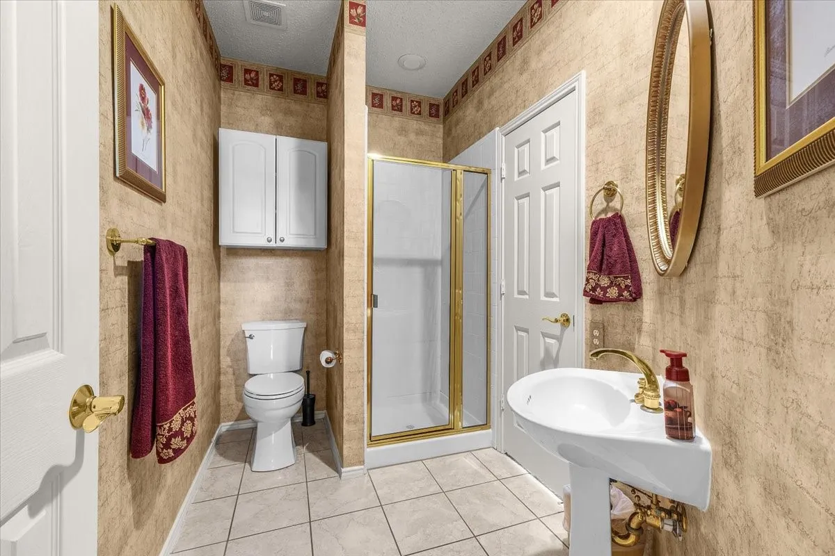Pedestal sink with brass-finish faucet, walk-in shower with gold-tone frame, white panel doors, and tile flooring