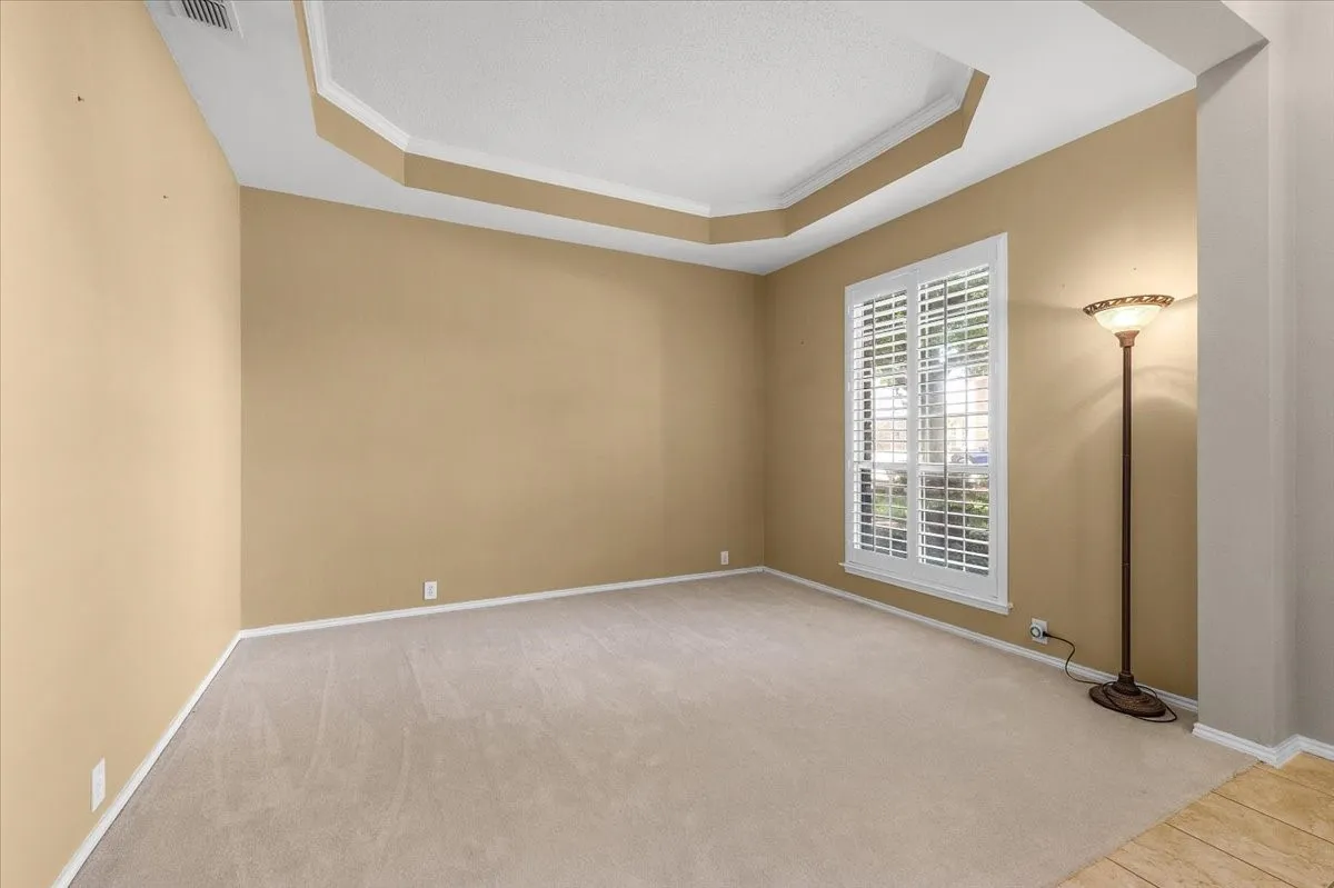 Tray ceiling with crown molding, carpeted flooring, and a window with plantation shutters