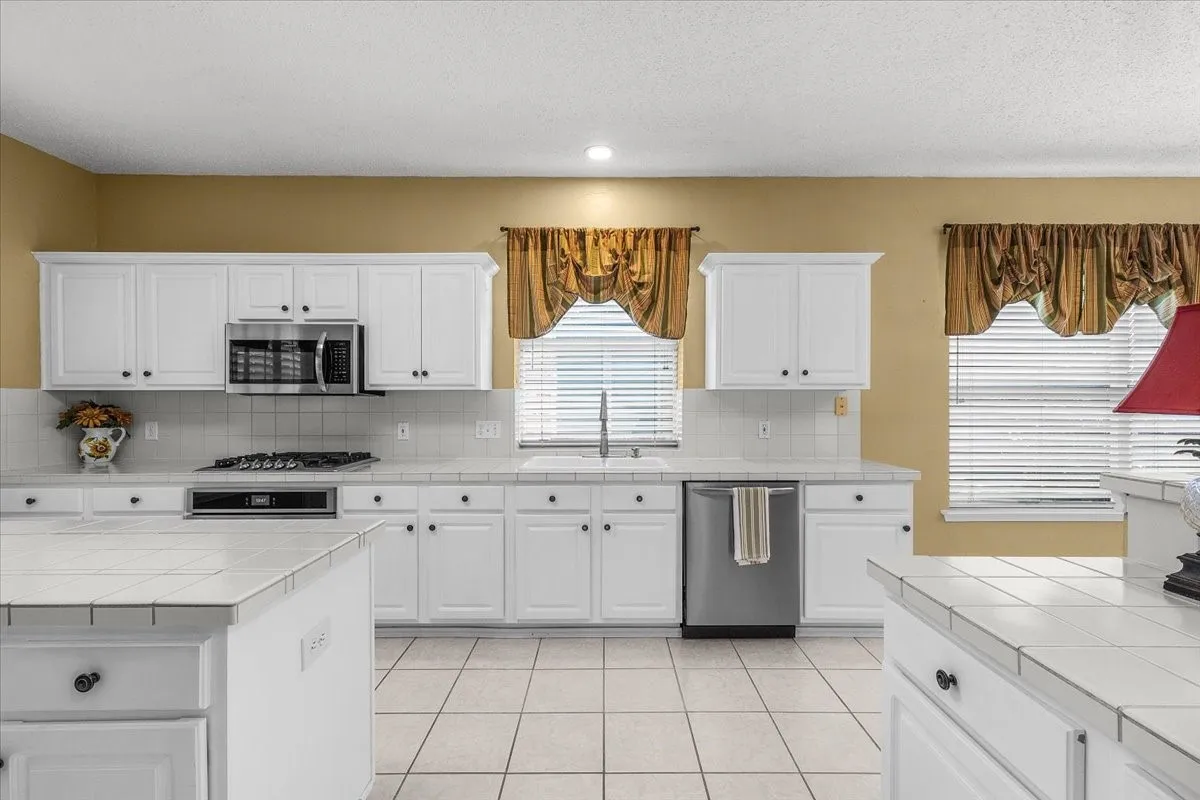 Kitchen featuring white cabinetry, tile countertops, stainless steel appliances, and tile flooring