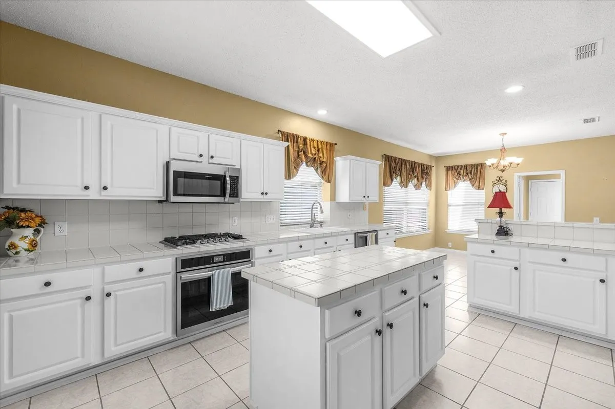 White cabinetry, stainless steel appliances, central island, tiled flooring, and recessed lighting