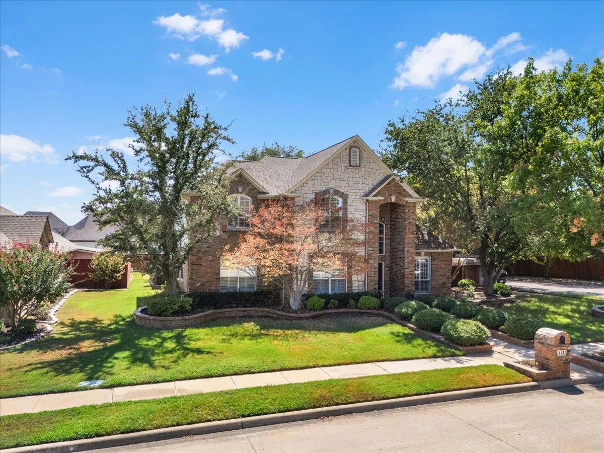 Brick and stone exterior, mature trees, landscaped front yard, concrete sidewalk, and a brick mailbox