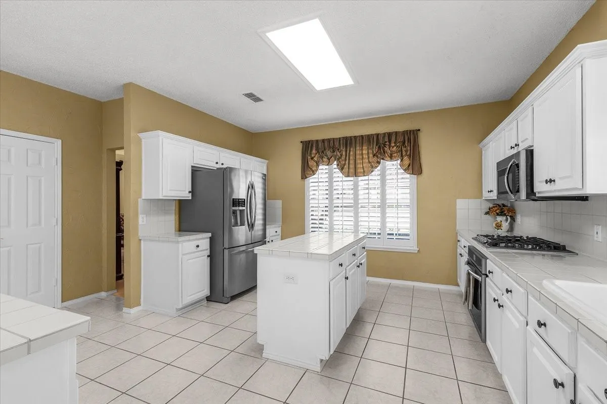 Kitchen featuring white cabinetry, a central island, tile flooring, and stainless steel appliances