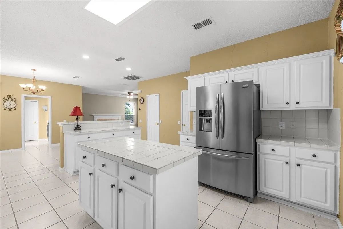 Kitchen with white cabinetry, tile countertops, stainless steel refrigerator, and recessed lighting