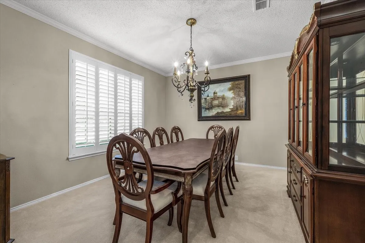 Window with plantation shutters, crown molding, and chandelier