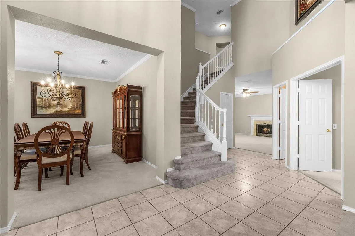 Two-story entry with tile flooring, grand staircase with carpeted treads, and prominent dining area with chandelier