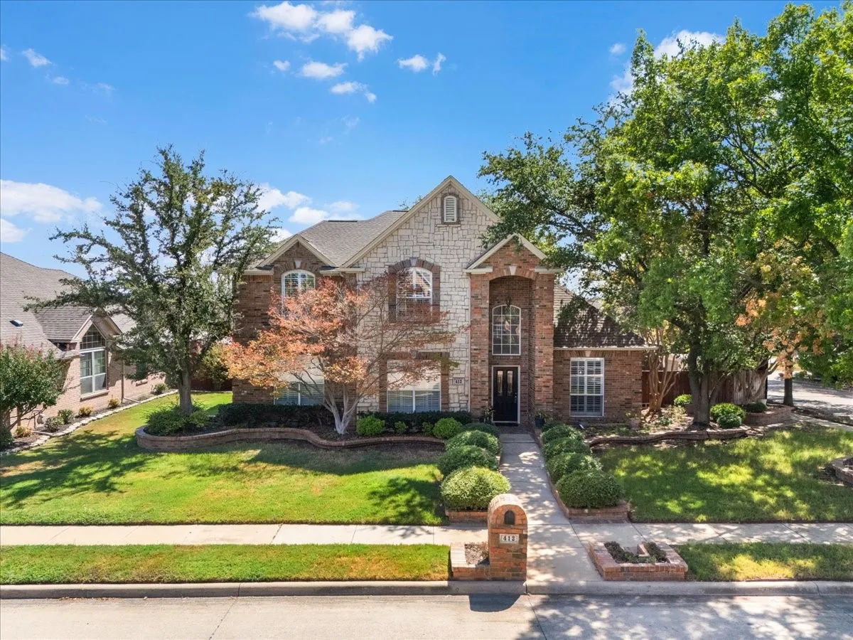Brick and stone exterior with arched windows, manicured landscaping, and a paved walkway leading to the entrance